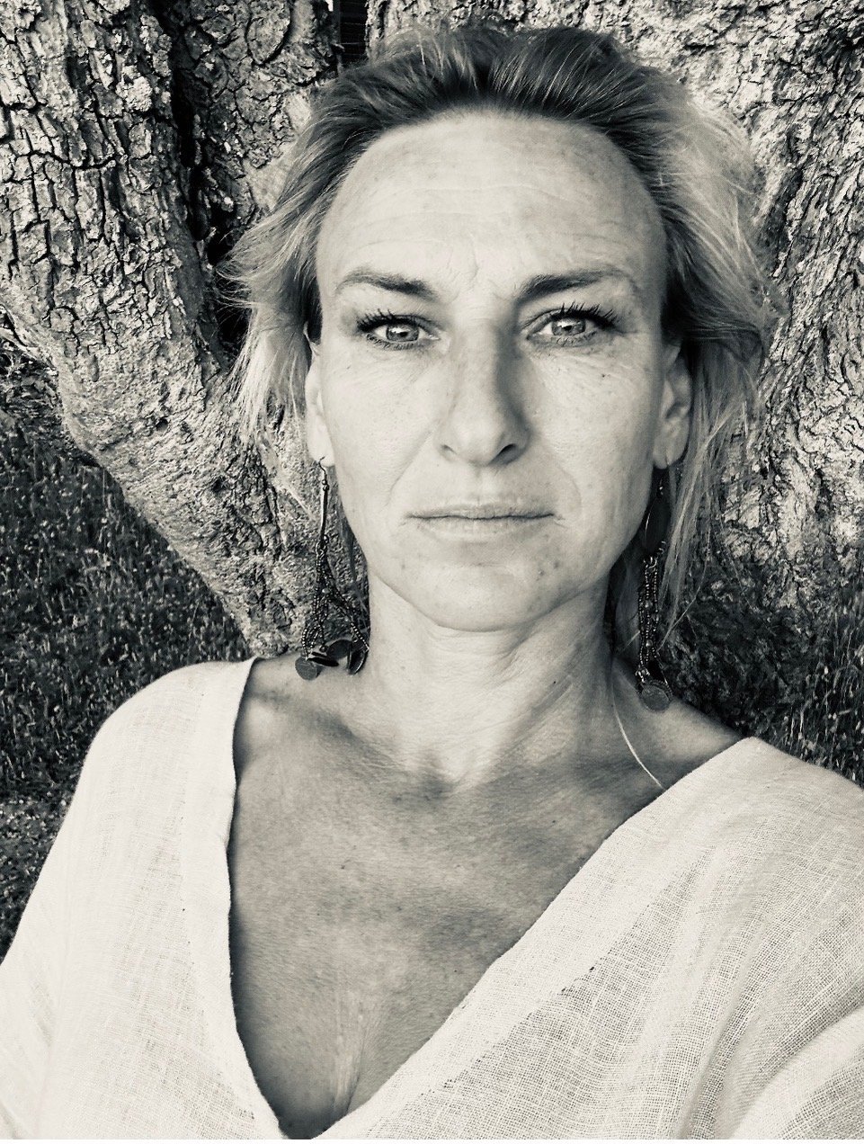 Black and white close-up photo of a woman with short hair, earrings, and leaning against a tree.