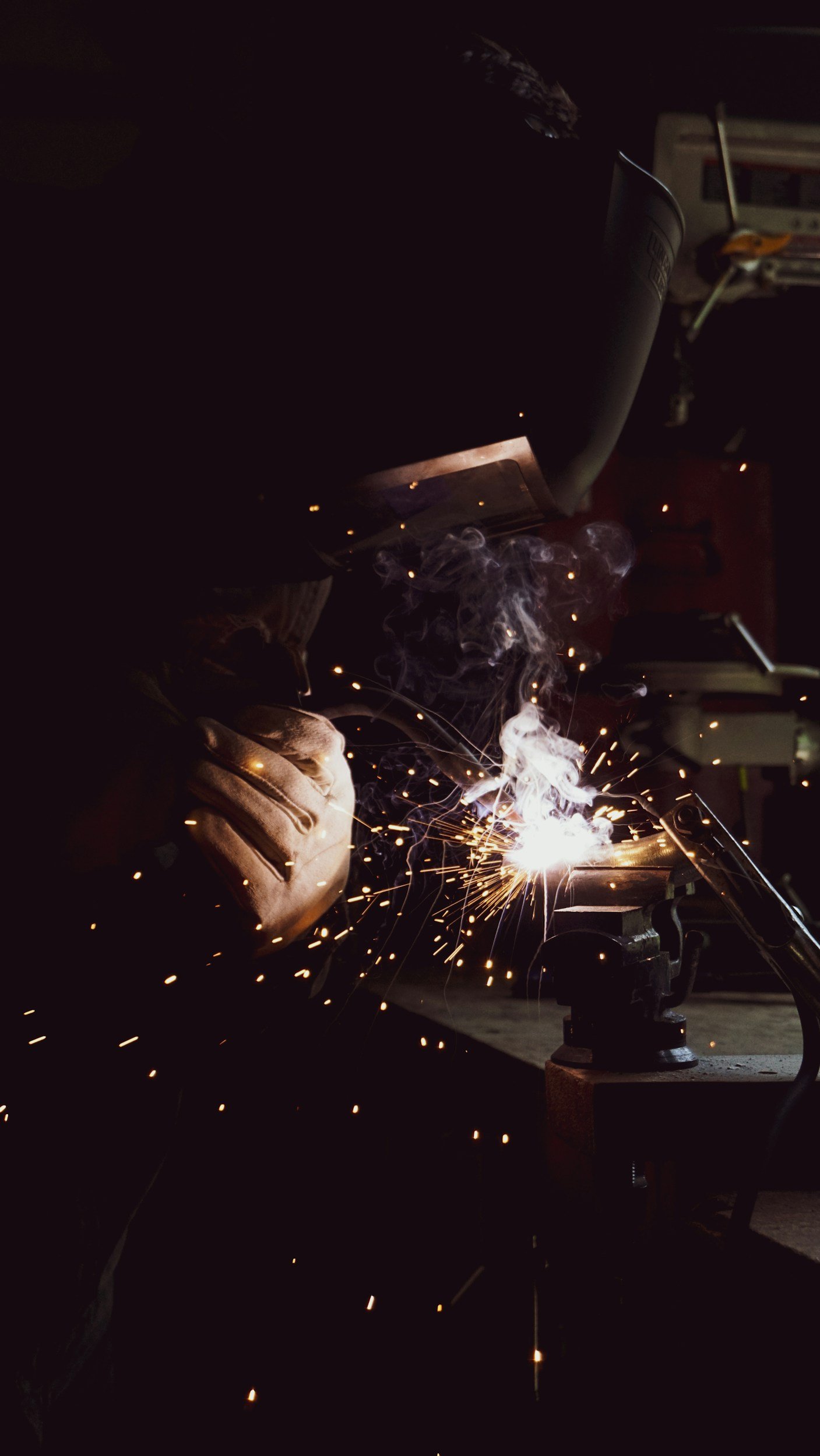 A person welding metal, creating sparks and smoke in a workshop.
