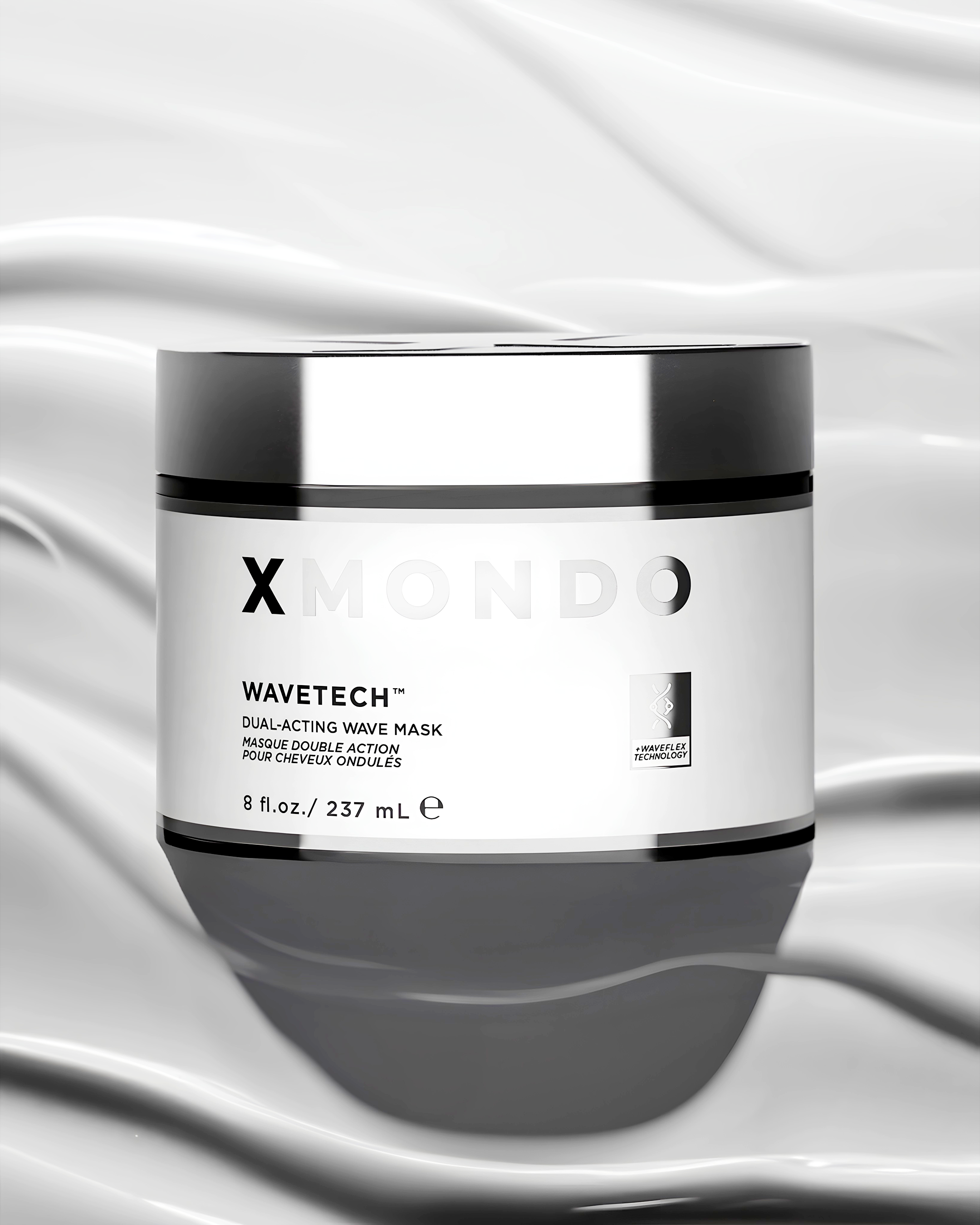 A black and white close-up of a skincare product container labeled 'X MONDO WAVETECH DUAL-ACTING WAVE MASK' with a white cap, set against a wavy, silky background.