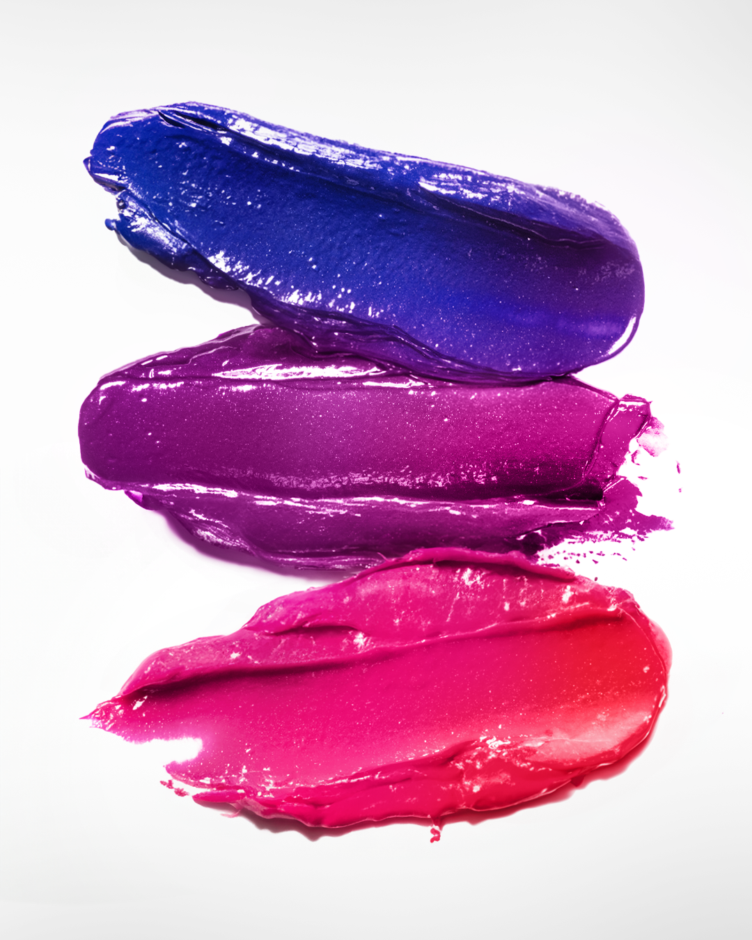Three smears of colorful lipstick in shades of blue, purple, and pink on a white background.