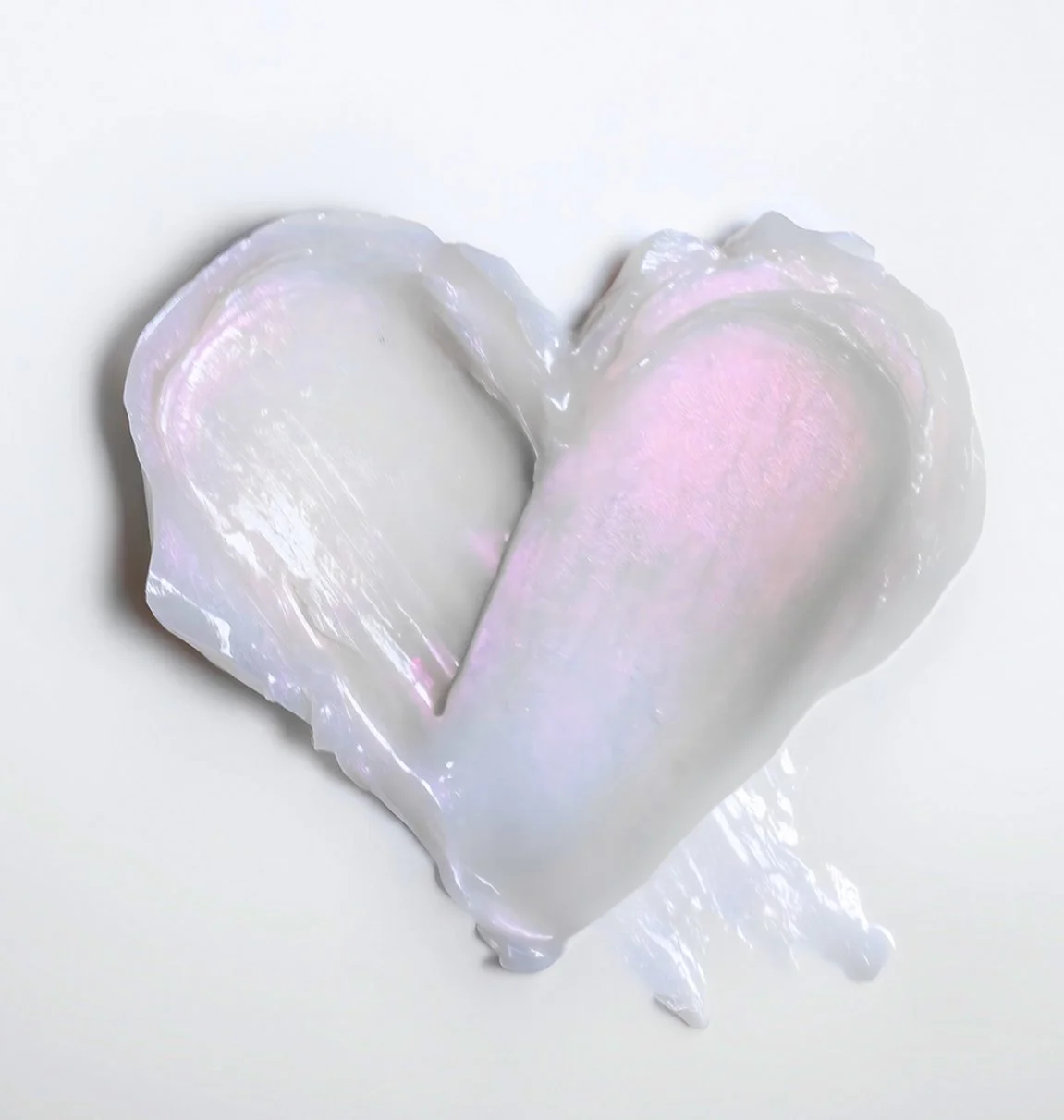 A broken heart shaped oyster shell with a shiny, iridescent surface and a hint of pink inside, set against a white background.