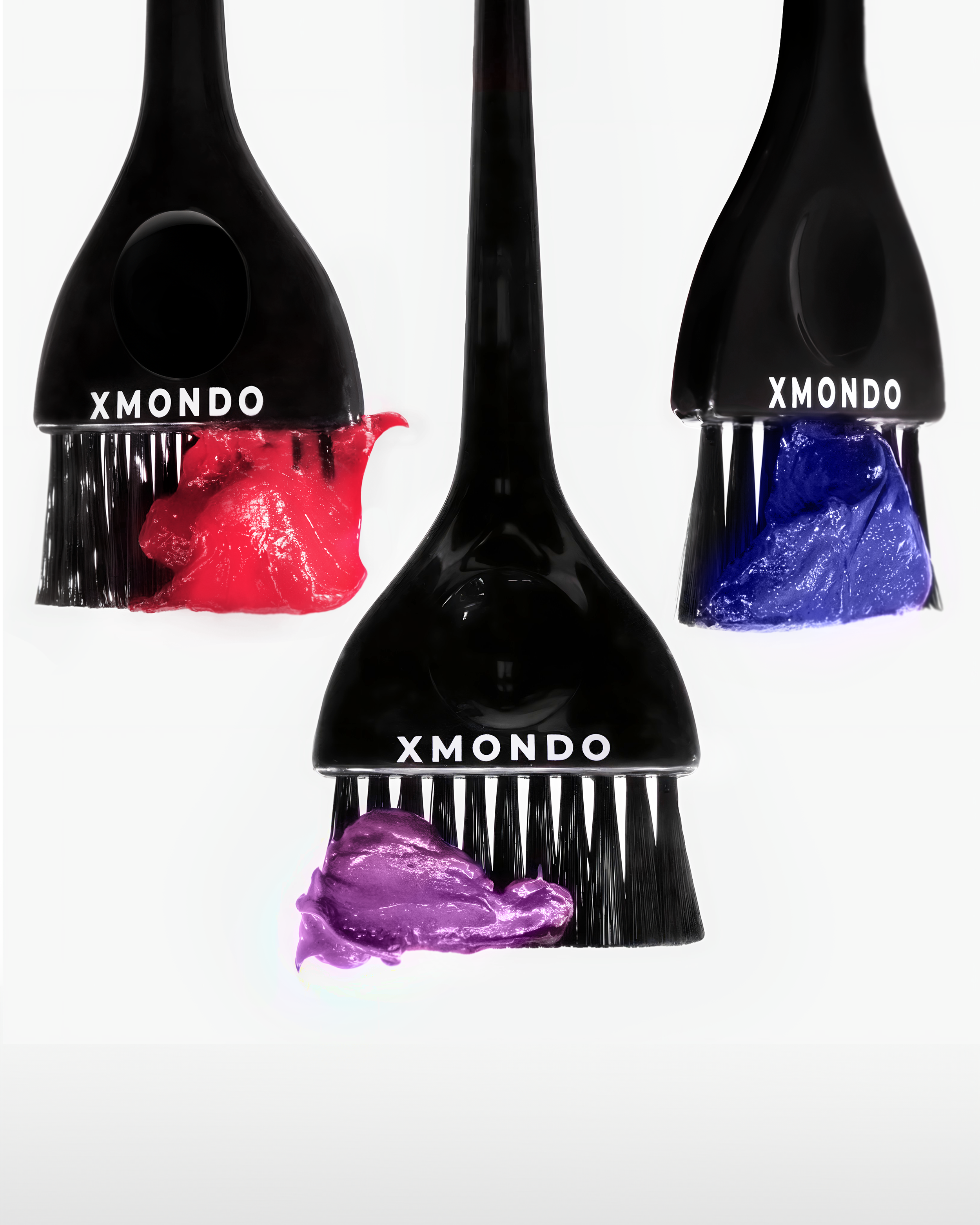 A black hairbrush with the word 'XMONDO' printed on it, with colorful blobs of hair dye—red, purple, and blue—around it, set against a white background.