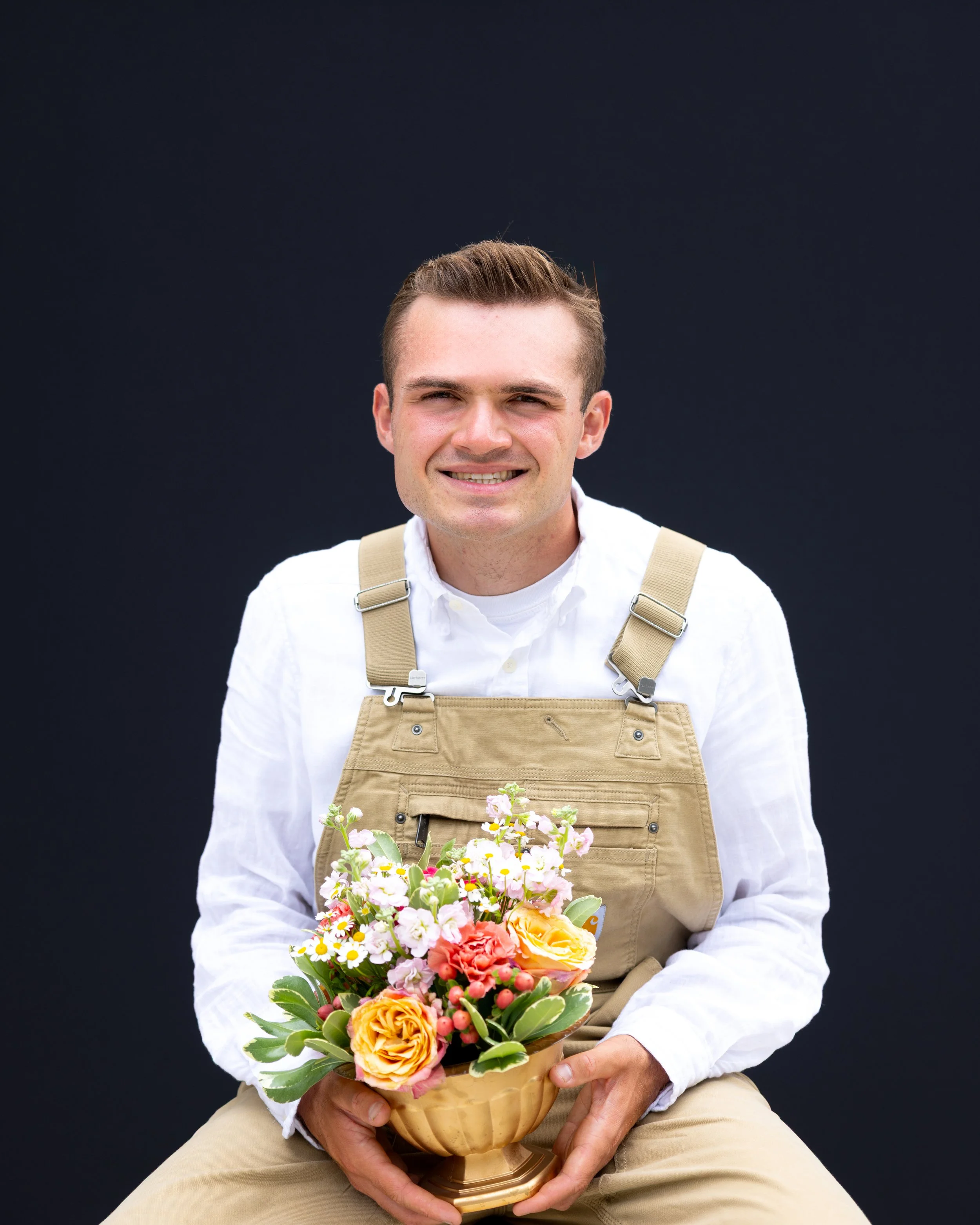 Sean from Petal & Garden holding a bouquet of pink, yellow, and white flowers in a small wooden basket.