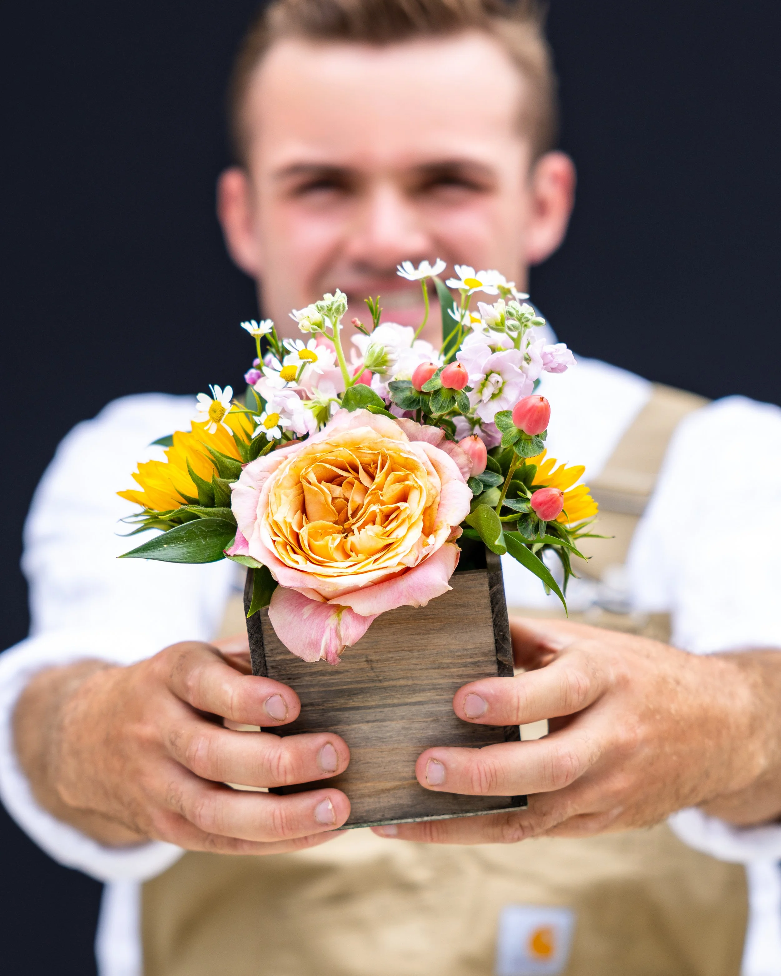 Sean holding a wooden display with a bouquet of colorful flowers, including roses, daisies, and other blooms.