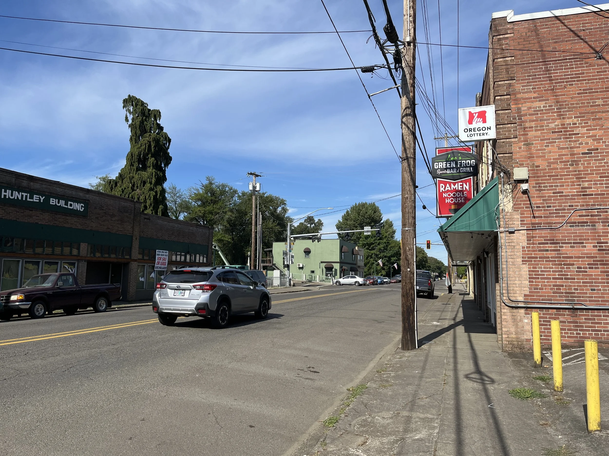 Street view with driving car, utility poles, and signs for restaurant and lottery. Blue sky with some clouds.