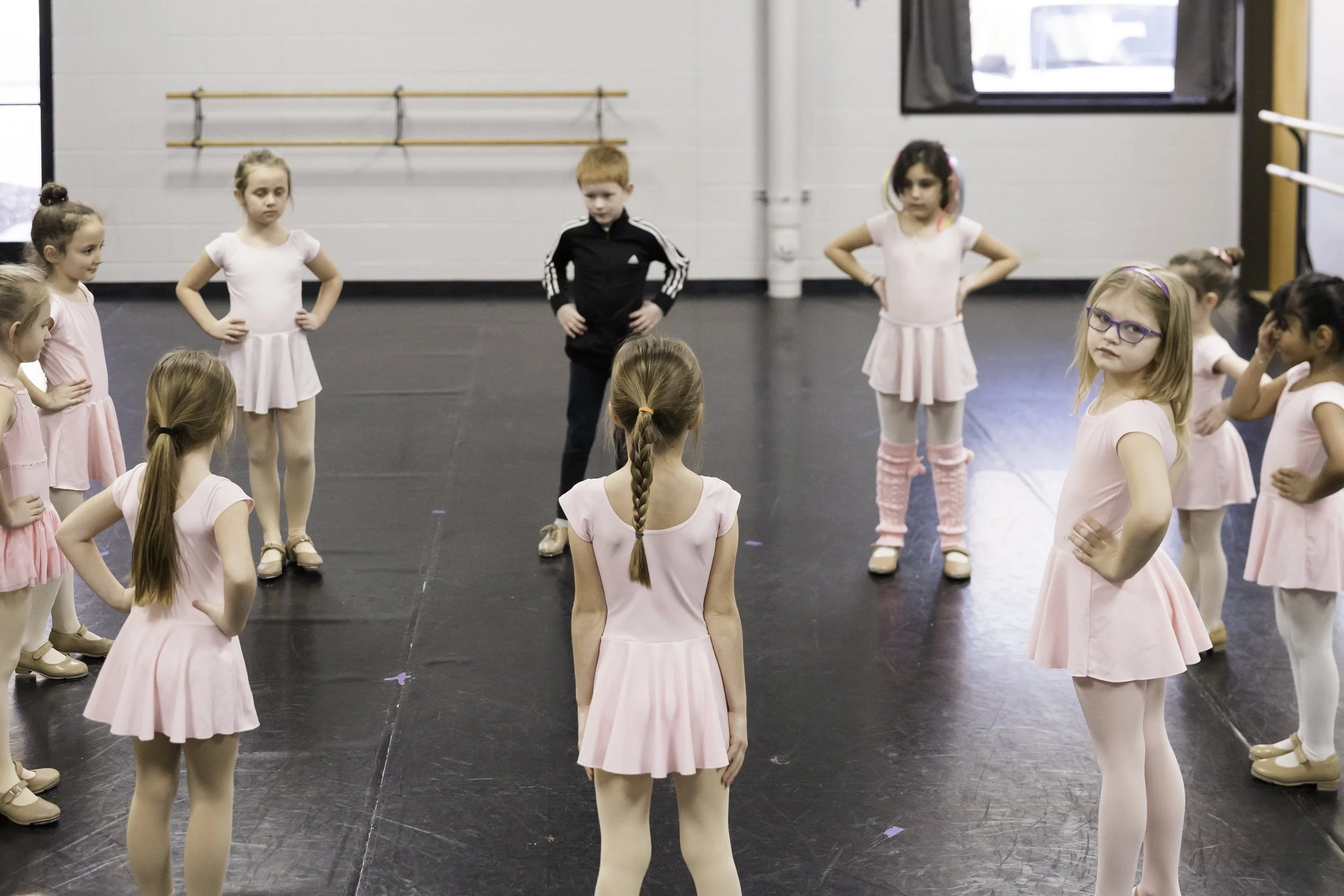 Children in ballet costumes standing in a circle in a dance studio.