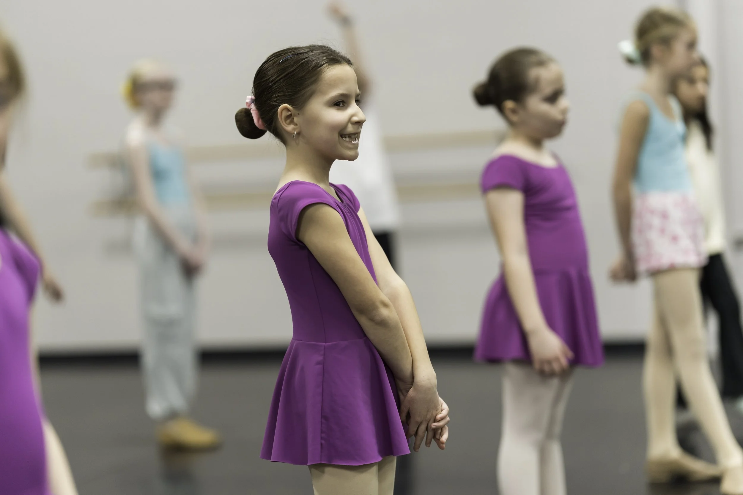 Young girls in colorful dance costumes practicing ballet in a dance studio.