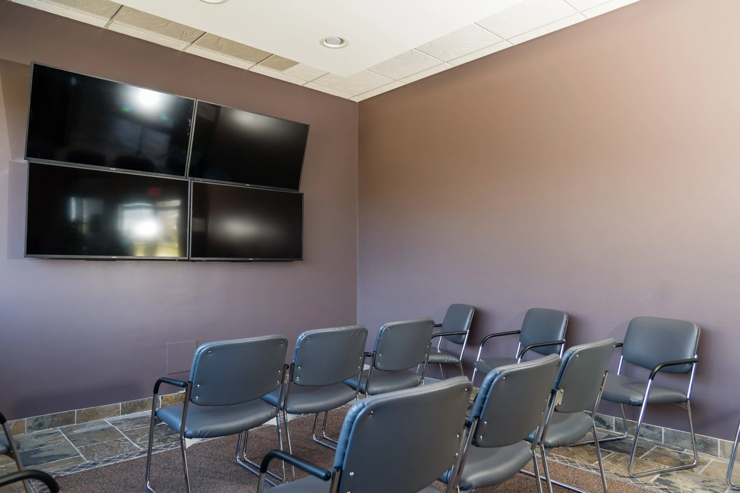Empty conference room with six gray chairs facing a wall-mounted television screen.