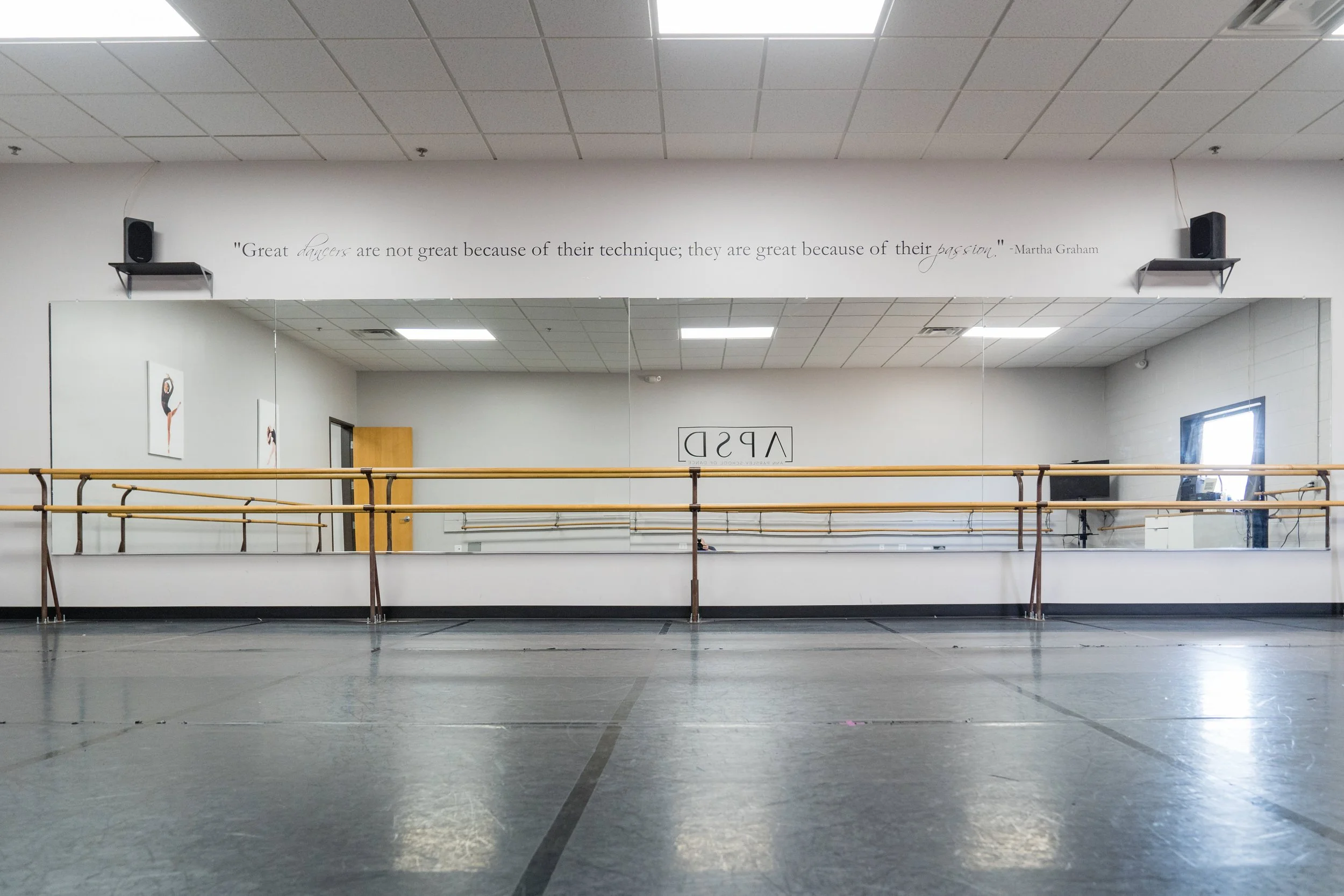 Dance studio with mirrors, ballet barres, motivational quote on the wall, and dance posters