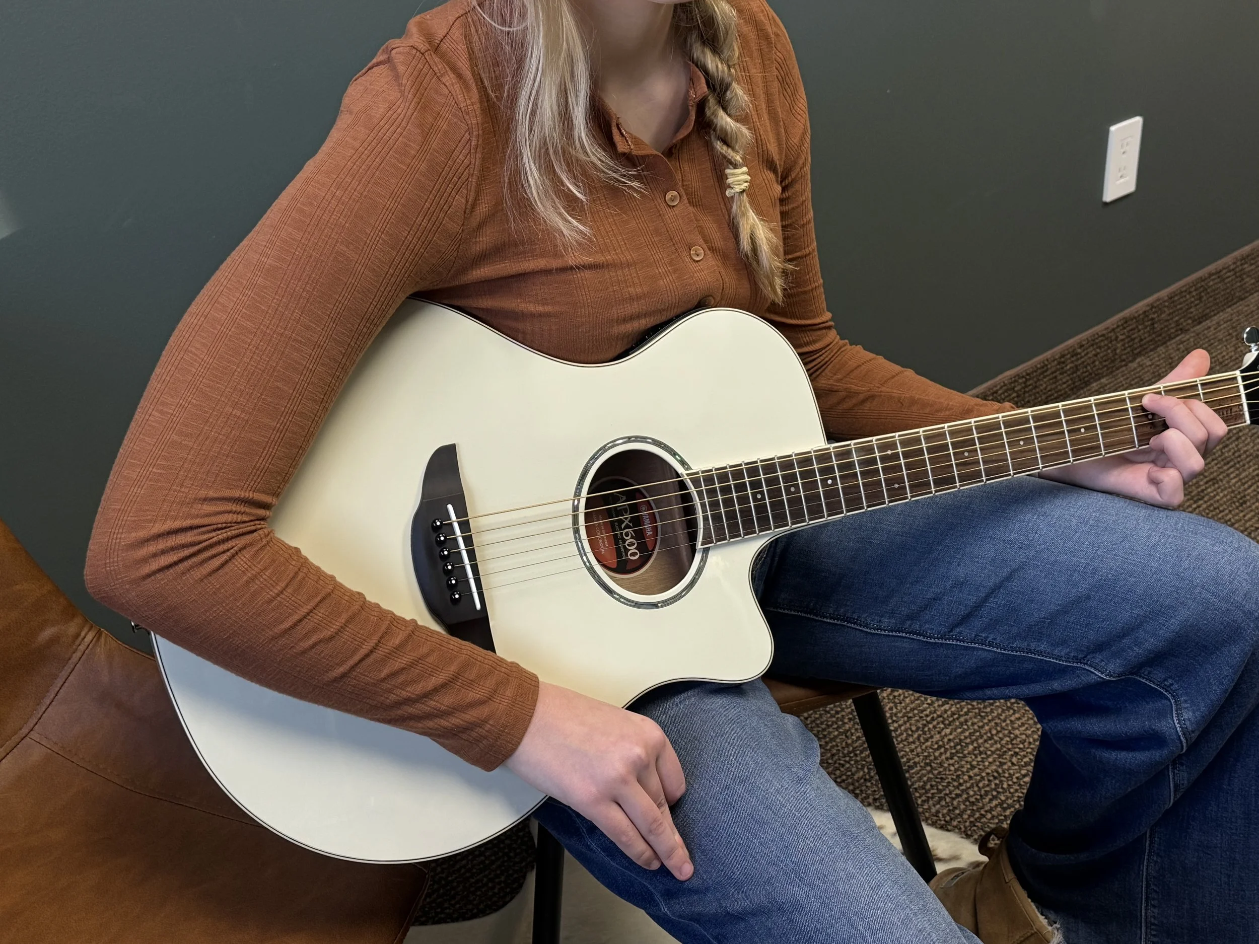 A child's hand on the strings of a black acoustic guitar with a wooden fretboard.