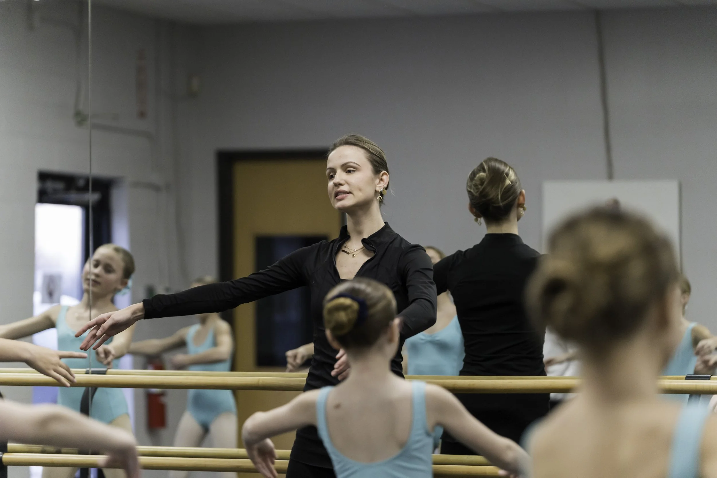 Ballet teacher instructing young dancers in a dance studio with mirrors.