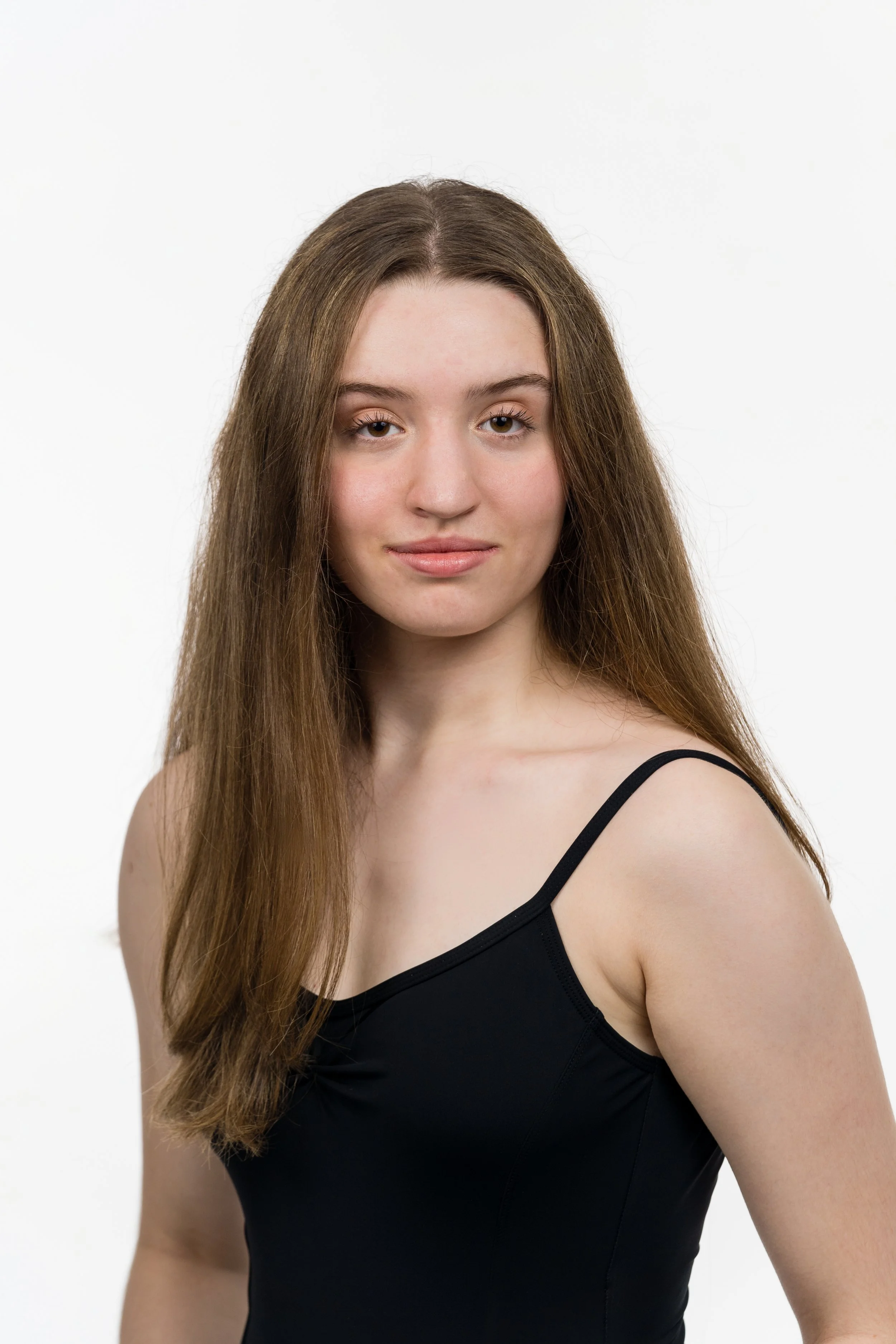 A young woman with long, straight brown hair wearing a black spaghetti strap top, standing against a plain white background.