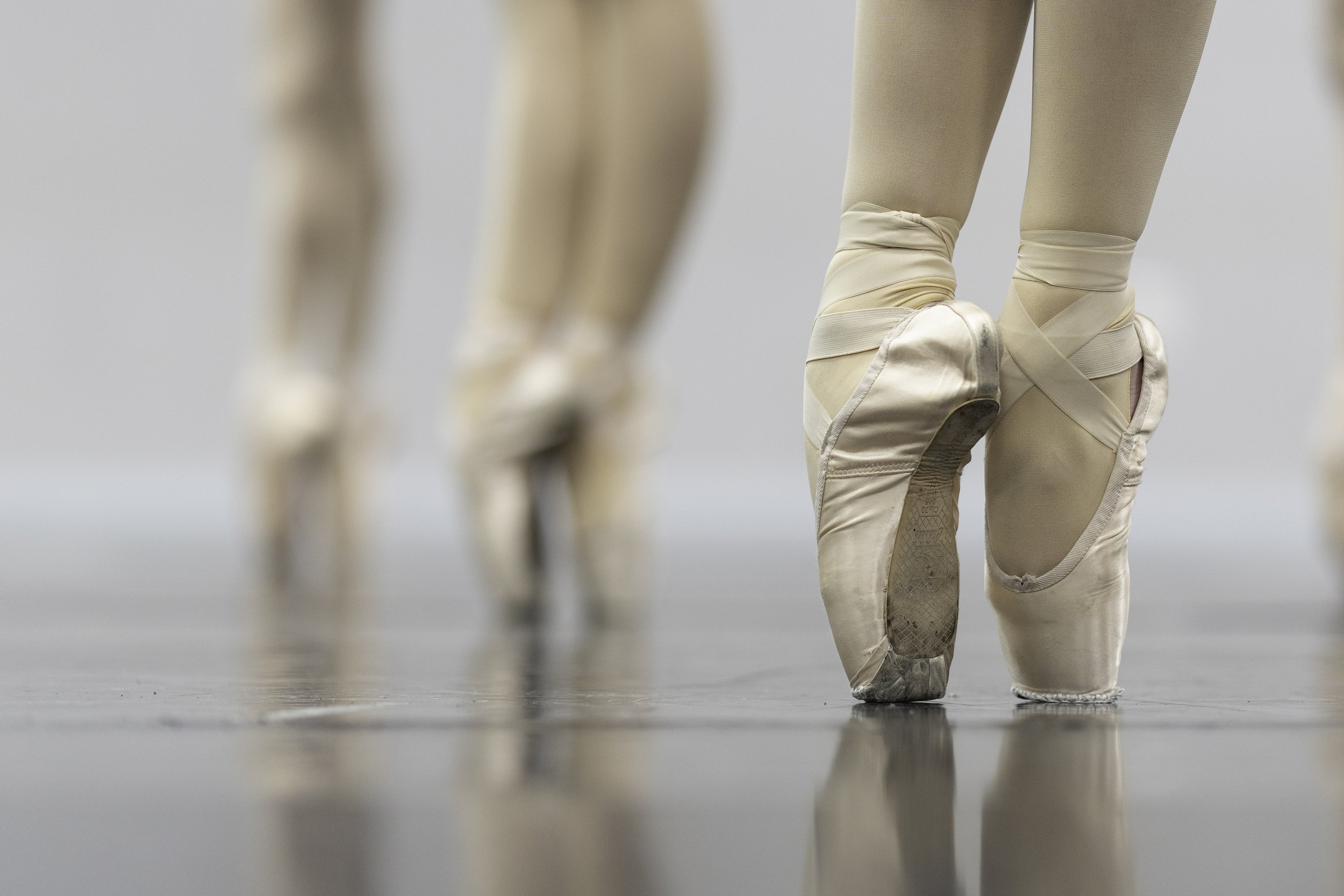 Close-up of ballet dancers' feet wearing pointe shoes, rehearsing in a studio.