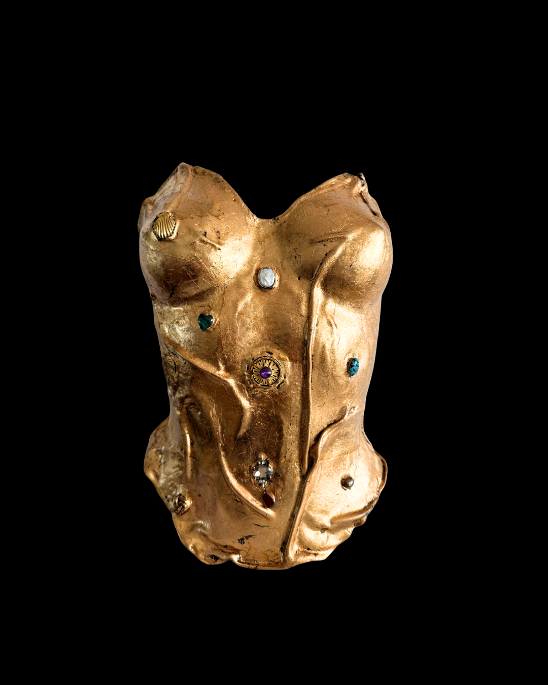 A gold-colored object resembling a human torso with various small, colorful gemstones embedded into it, displayed against a black background.