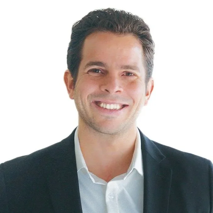Nick Ortner in a black blazer and white shirt smiling against a white background.
