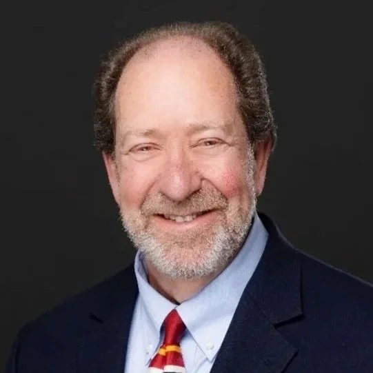 David Eisenberg, MD wearing a dark navy suit, light blue shirt, and a colorful striped tie, against a black background.