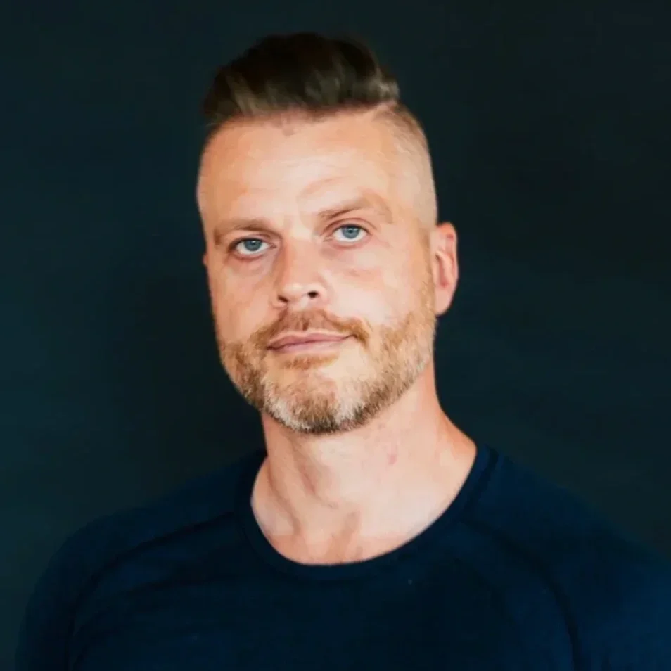 David Magone wearing a dark shirt, against a dark background.