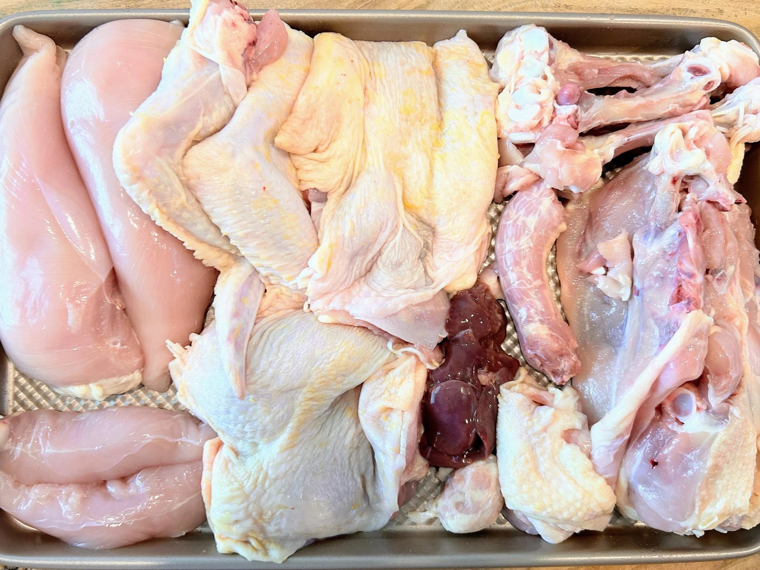 Assorted raw chicken cuts including breast, thighs, drumsticks, and wings arranged in a tray.