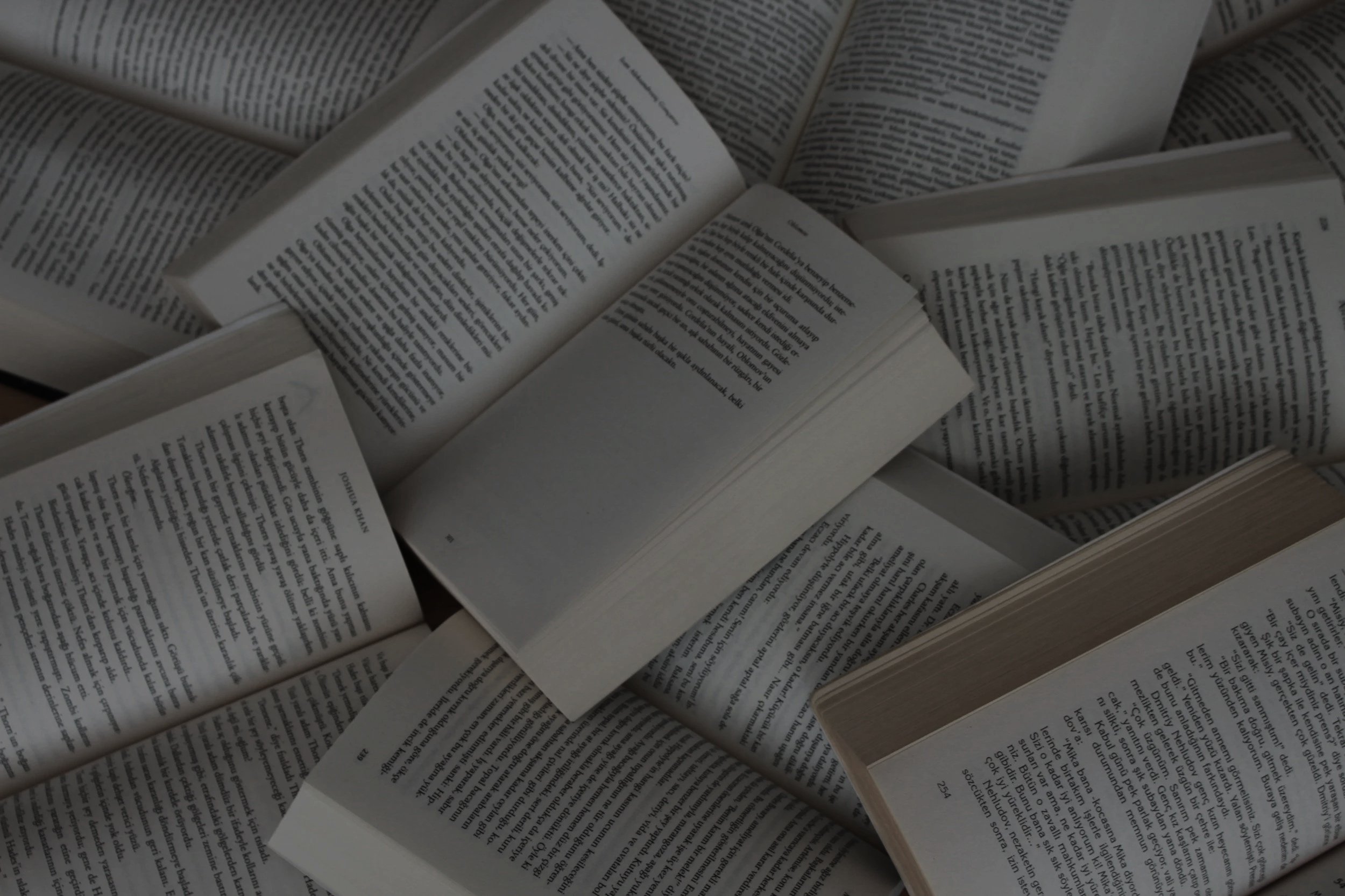 Multiple open books with text visible on white pages, stacked and overlapping each other.