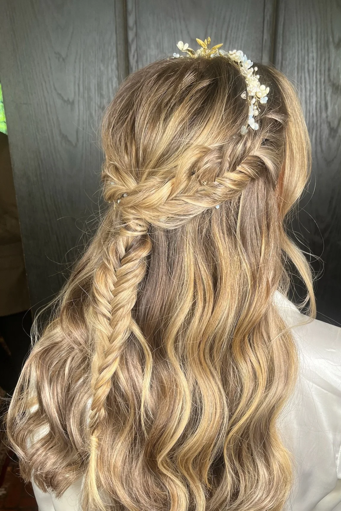 Side view of a woman with long wavy blonde hair styled with a twisted braid across the back and a pearl and floral hair accessory.