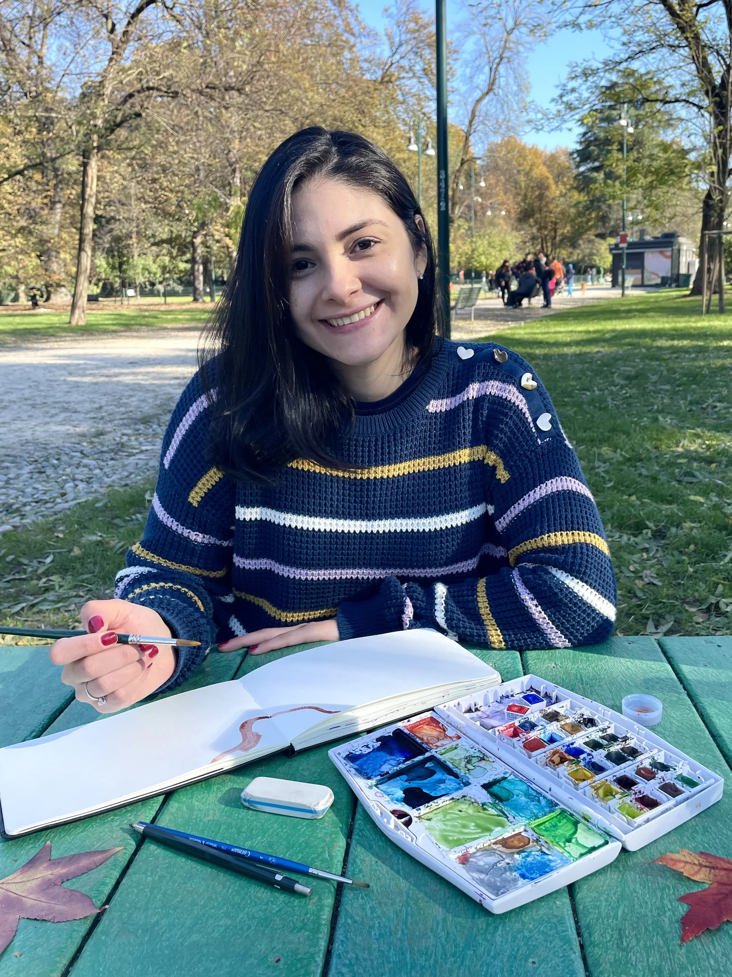 Carlissima pintando con acuarela rodeada de pinceles, colores y materiales de ilustración