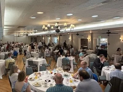 A large banquet hall filled with round tables set for a meal, with many people seated and dining.