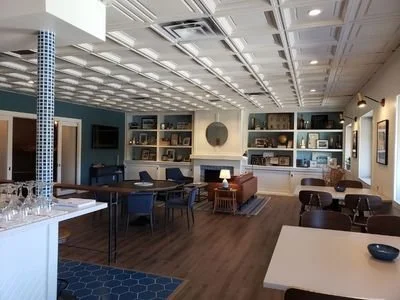A spacious room with a ceiling grid, built-in shelves with decor, and multiple seating arrangements including chairs and sofas.