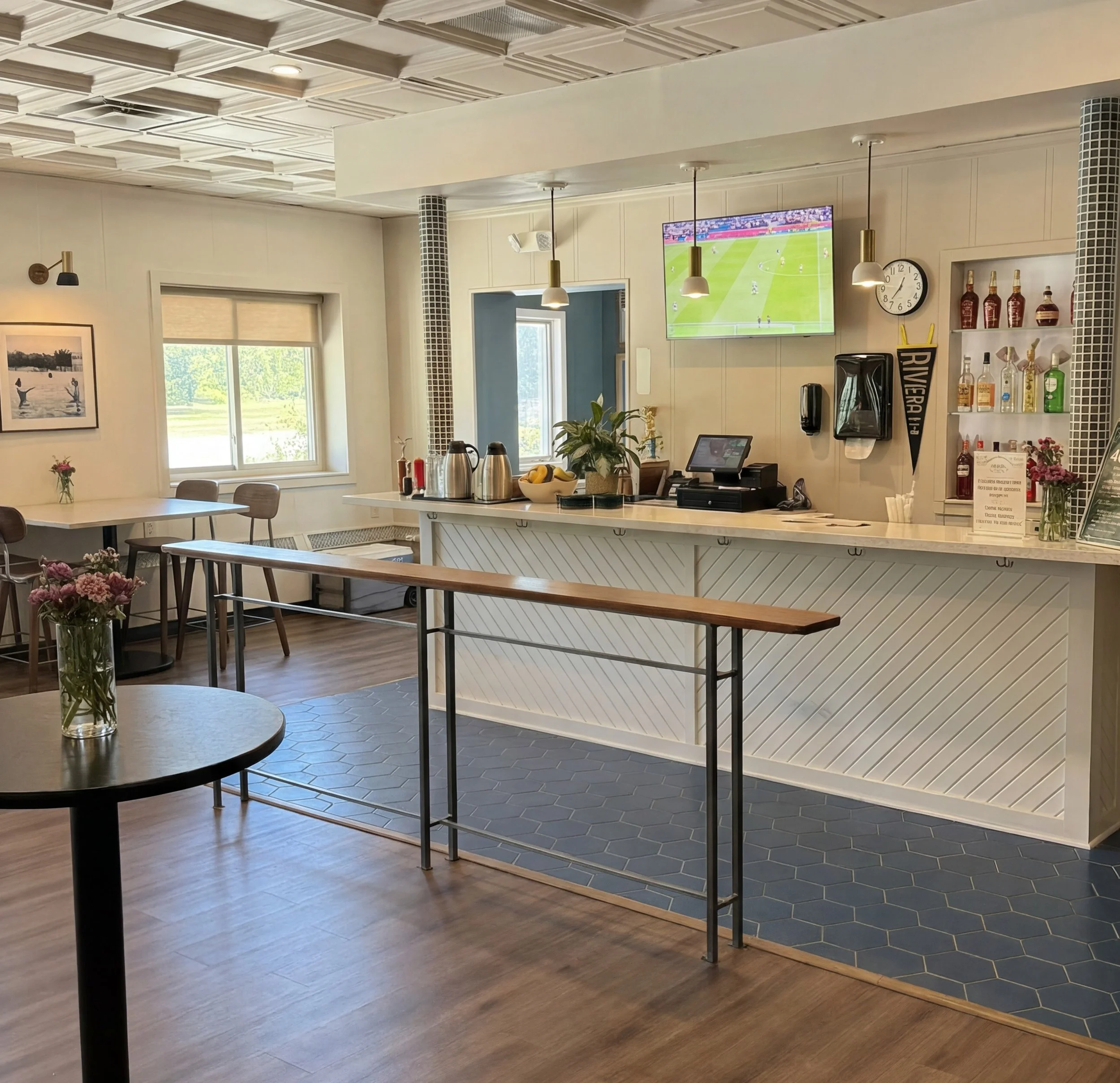Interior of a cozy cafe or restaurant with a counter, TV showing a soccer game, and dining area with tables and chairs.