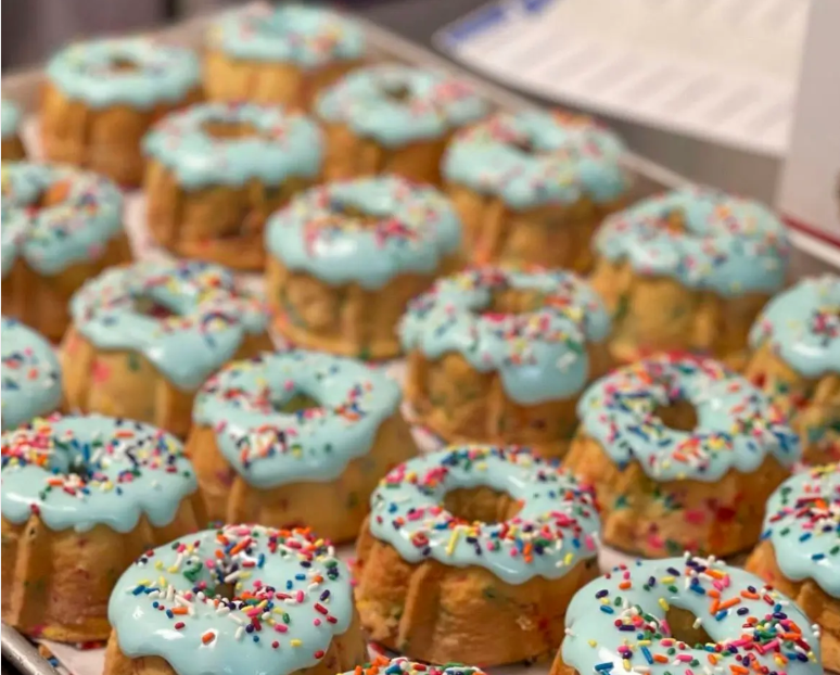 Tray of mini donuts topped with light blue icing and colorful sprinkles.