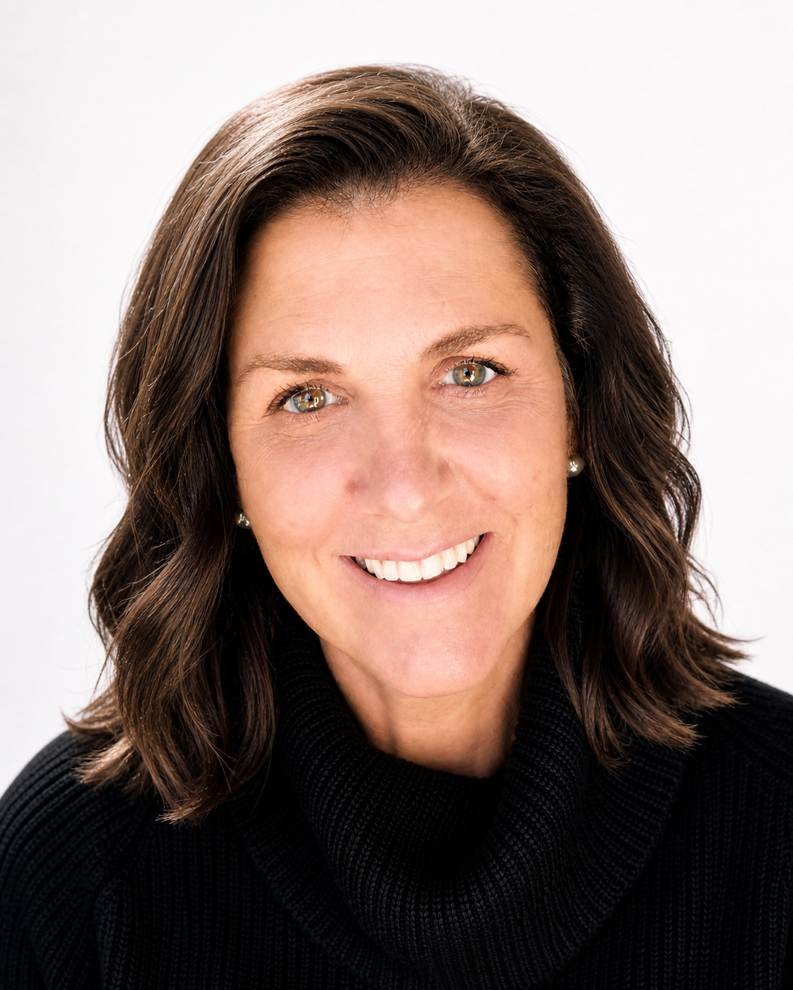 Close-up portrait of a smiling woman with shoulder-length brown hair, wearing a black turtleneck sweater and pearl earrings.