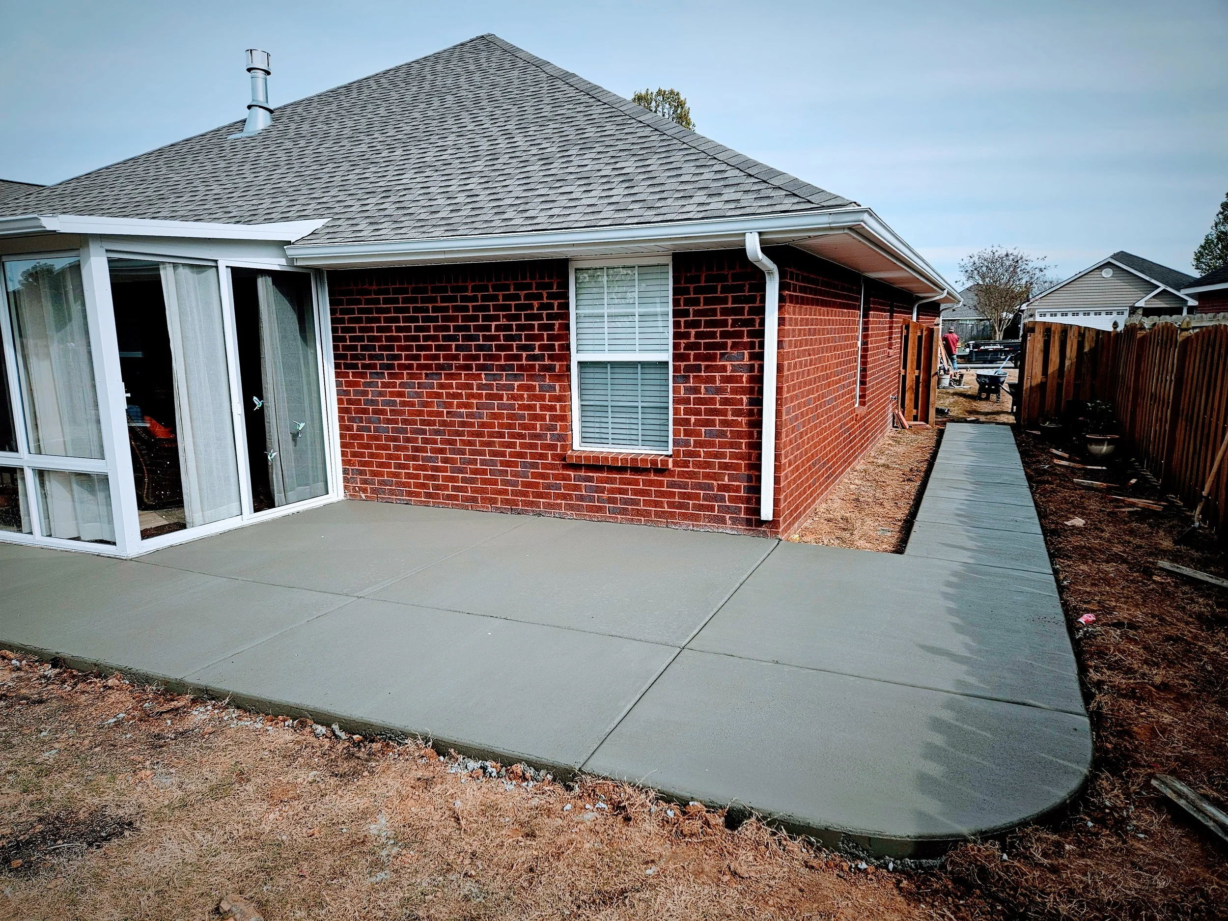 New concrete patio with sliding glass door on a brick house, backyard with wooden fence, and construction tools.