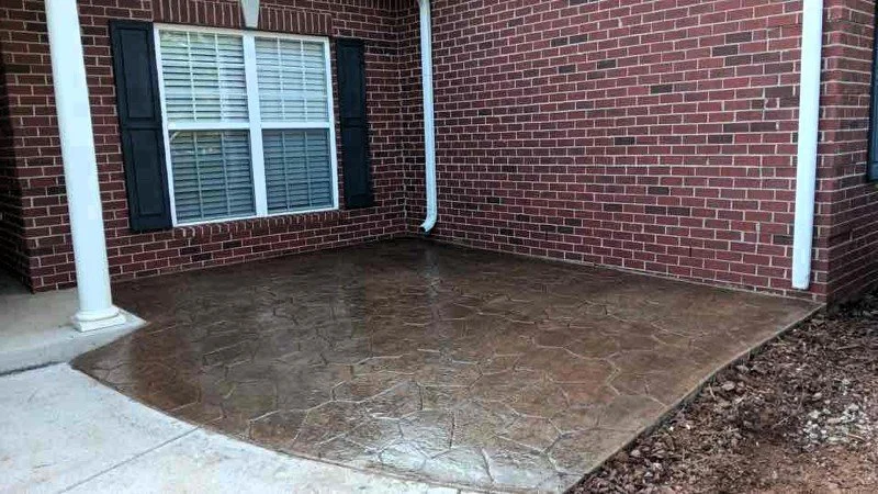 Newly poured and stamped concrete patio in front of a brick house with a window and black shutters.