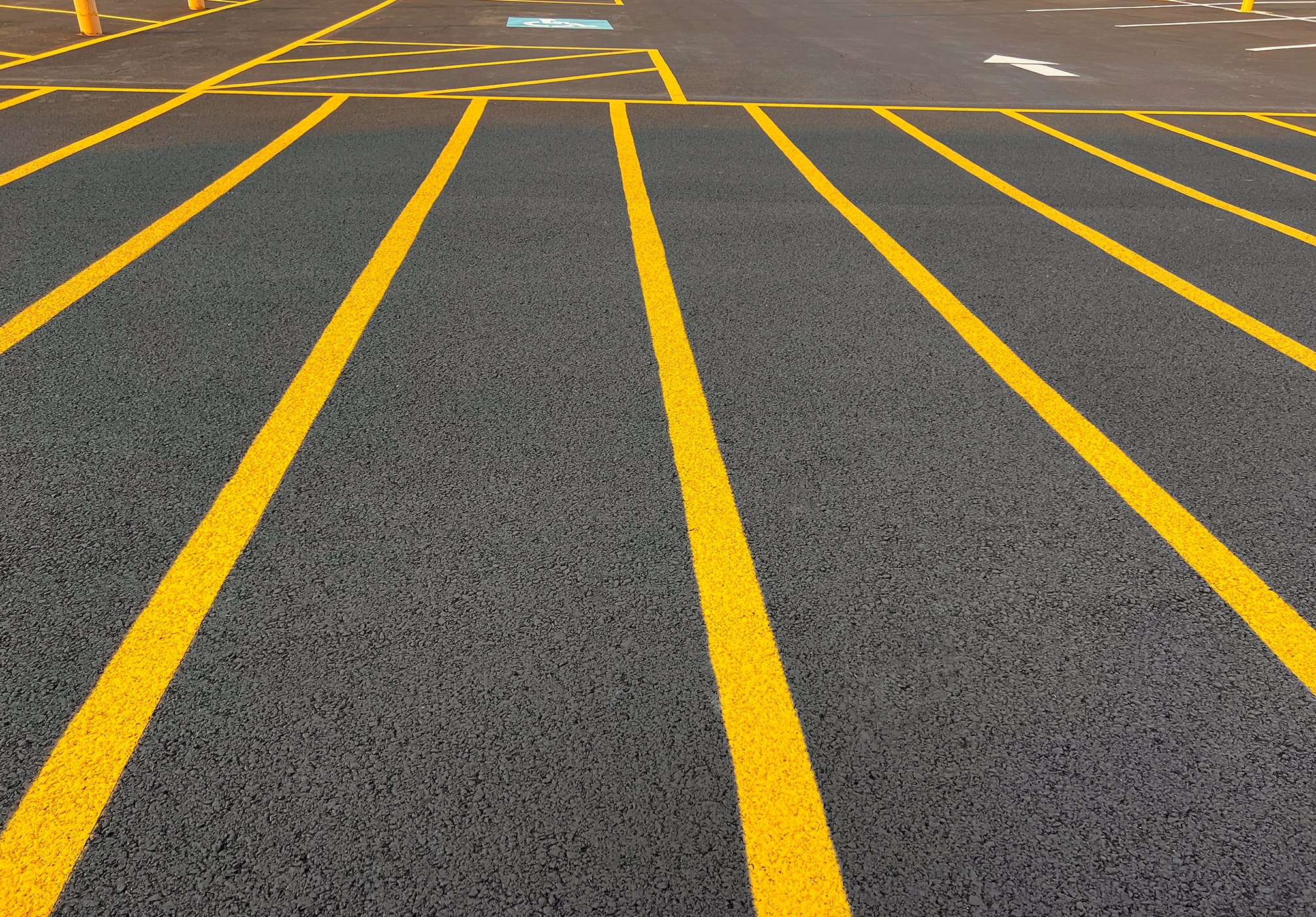 Empty parking lot with crisp yellow painted lines and a blue handicapped parking sign on asphalt.