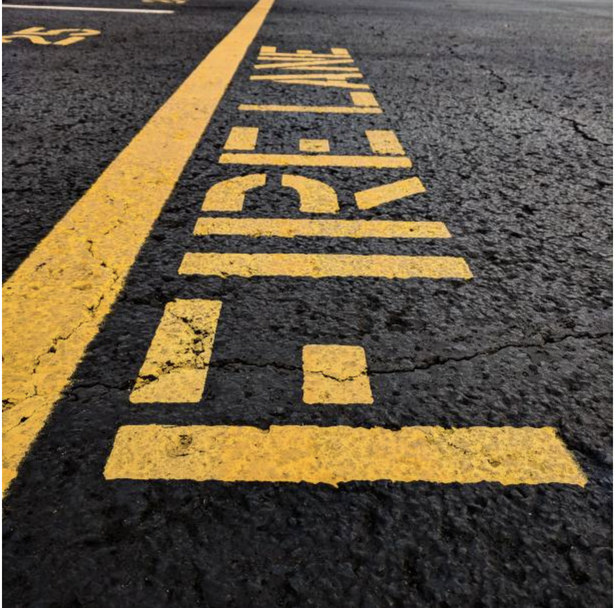A close-up view of a yellow line and the word 'STOP' painted on asphalt pavement.