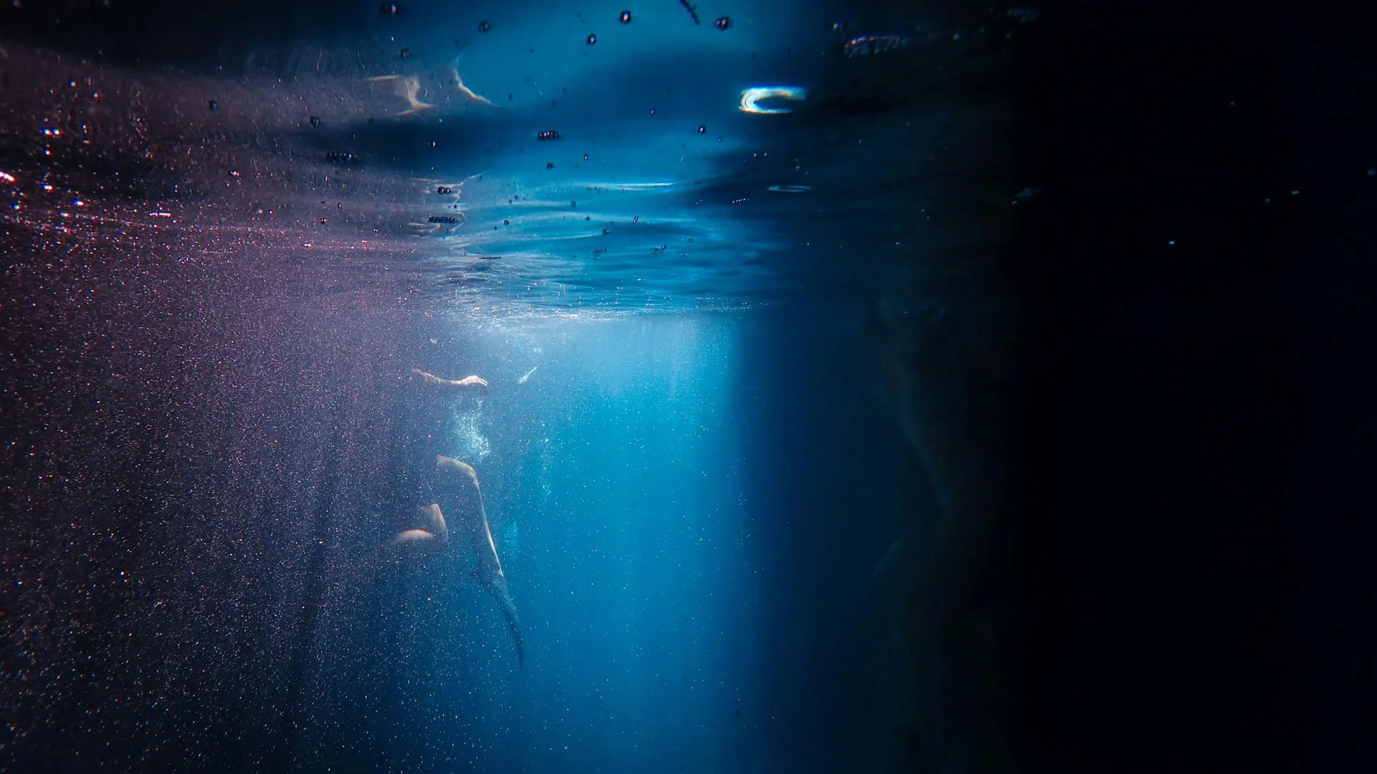 Underwater view with bubbles and a person swimming, illuminated by a blue light