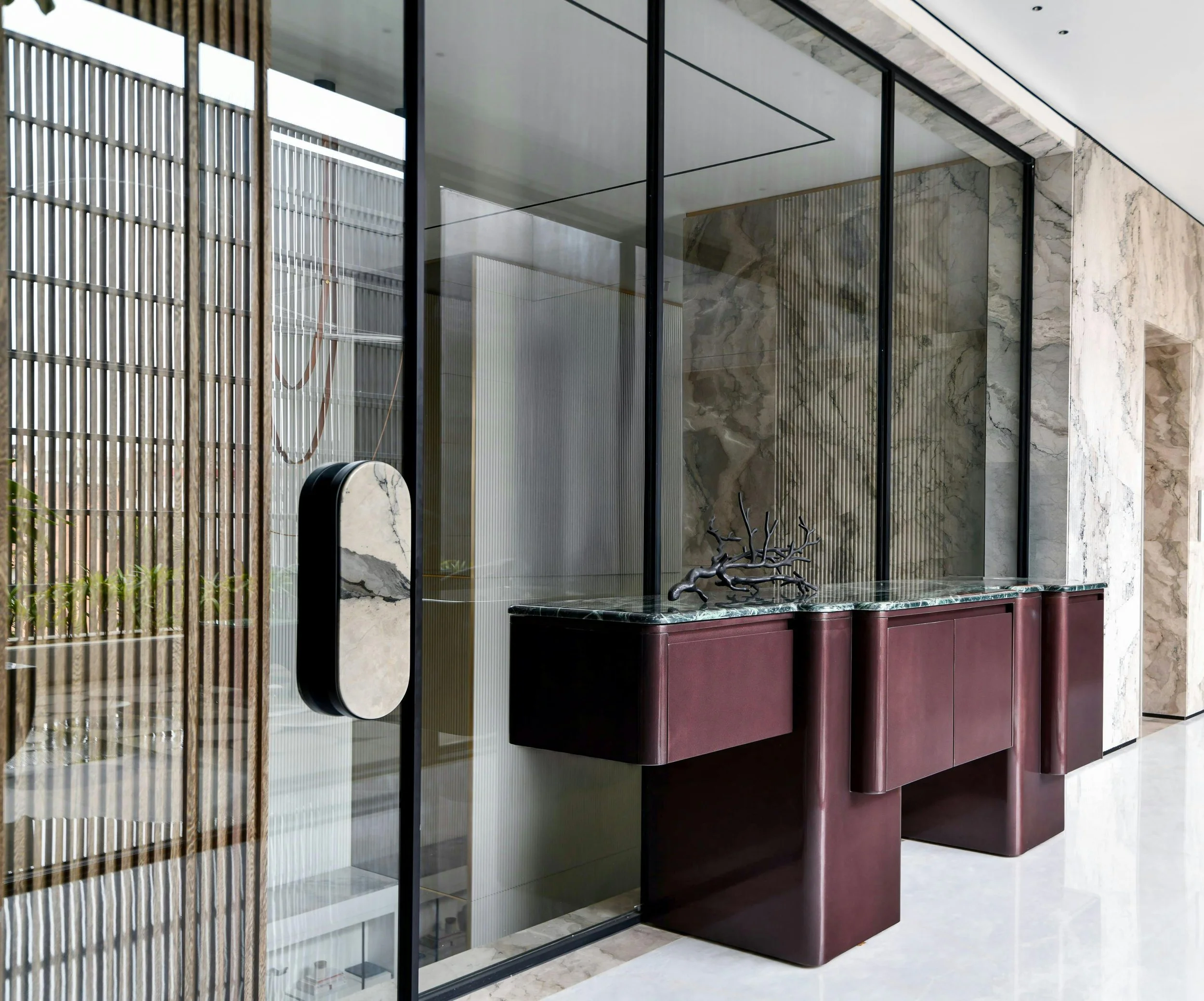 Interior view of a modern building with glass walls, marble finishes, and a decorative sculpture on a maroon cabinet.