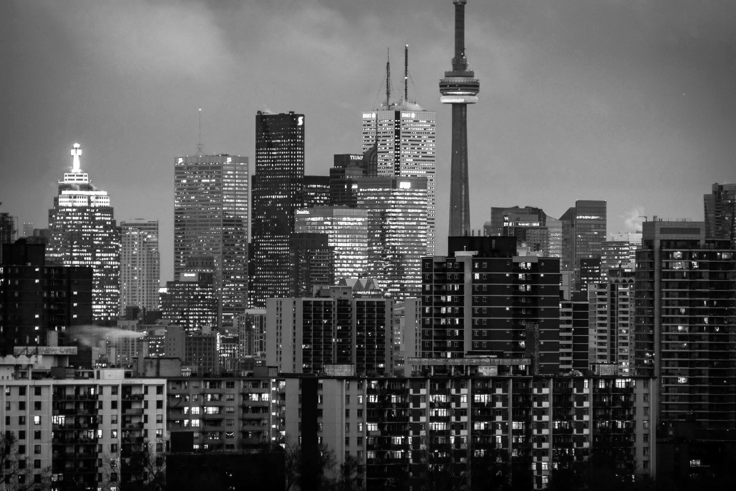 Dark cityscape featuring tall illuminated skyscrapers and high-rise buildings at night.