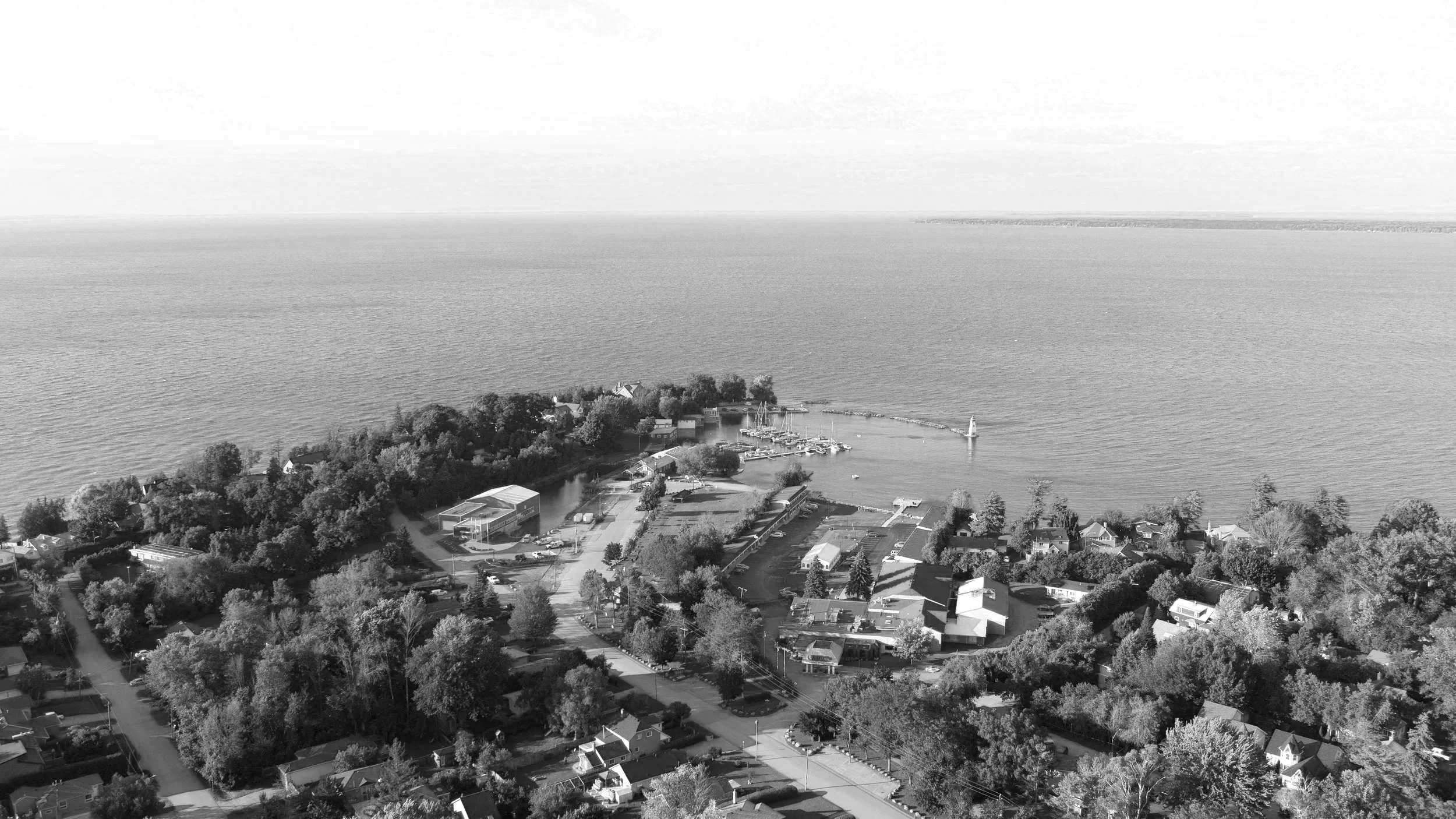 Aerial view of a lakeside residential area with boats, trees, houses, and a sailboat on the water, in black and white.