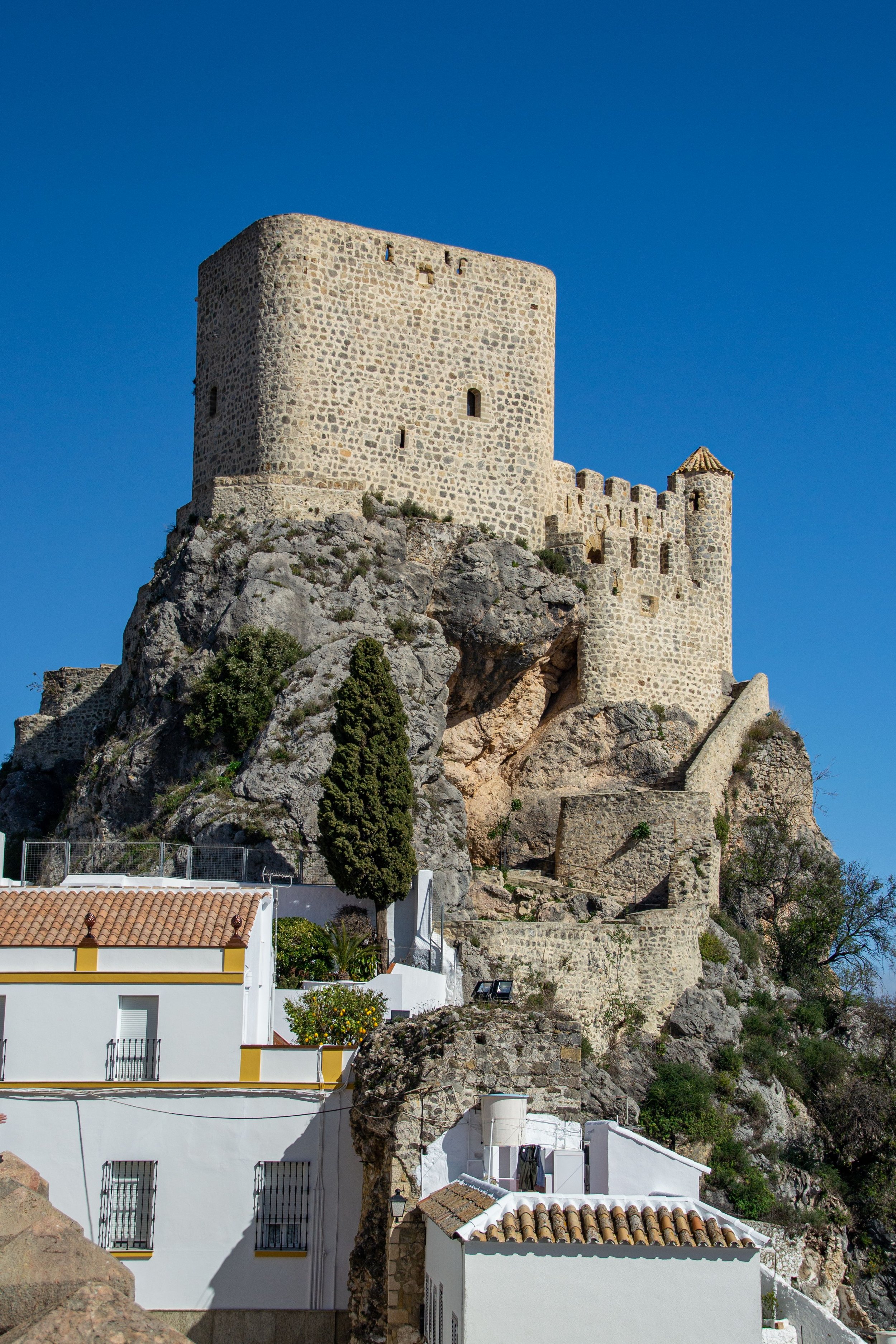 Historic stone fortress tower perched above a hillside village on the Mediterranean coast of Spain.