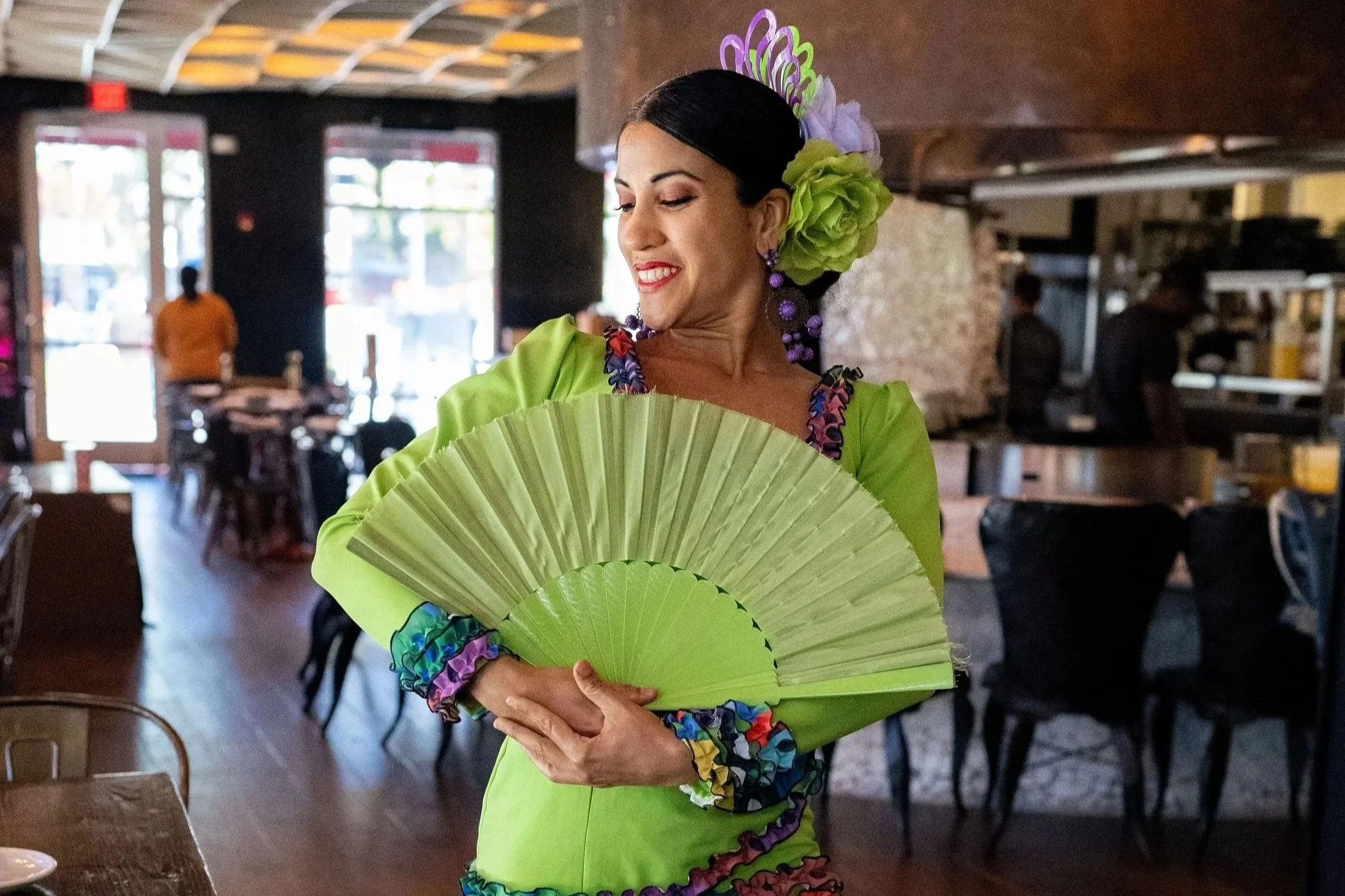 Experiencing authentic Spanish culture, posing in a traditional Flamenco dress with a green folding fan and bright hair flowers.