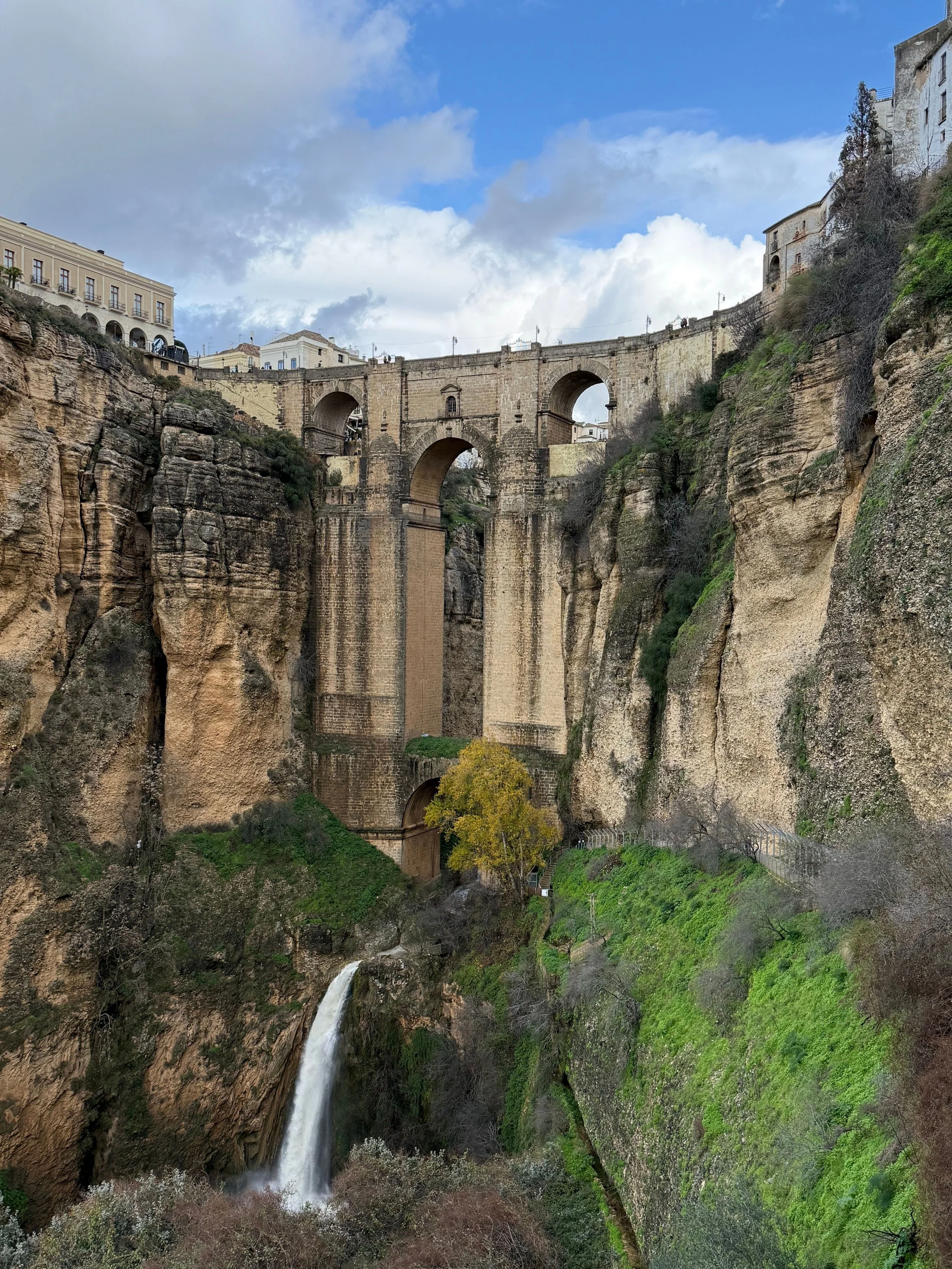 Historic Puente Nuevo stone bridge spanning the deep El Tajo gorge with a waterfall cascading below in Ronda, Spain.