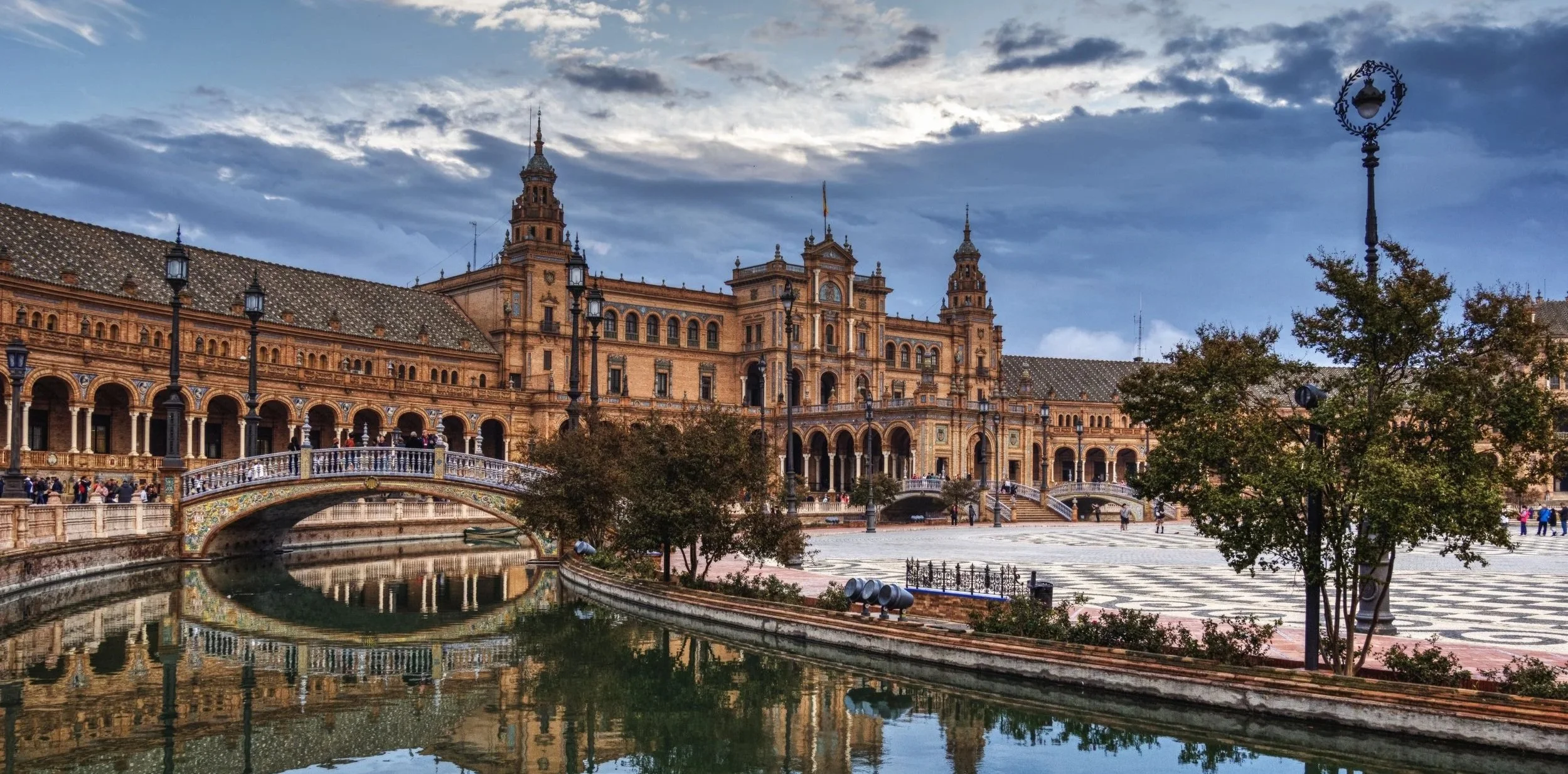 Alt Text: Grand panoramic view of Plaza de España in Seville with its tiled bridges, central canal, and historic pavilion.