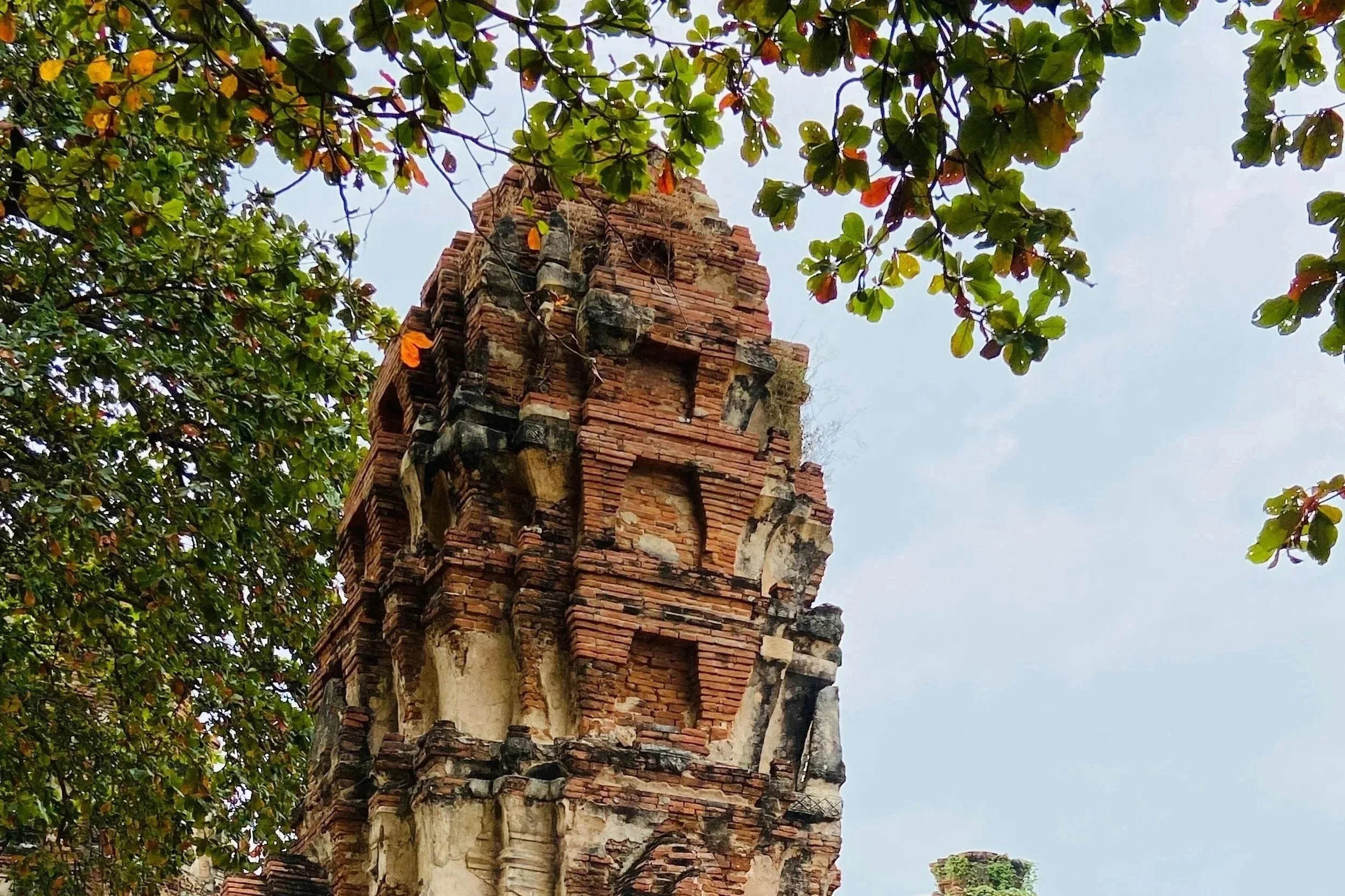 Catching a glimpse of an ancient brick and stone tower framed by lush green branches under cloudy skies.