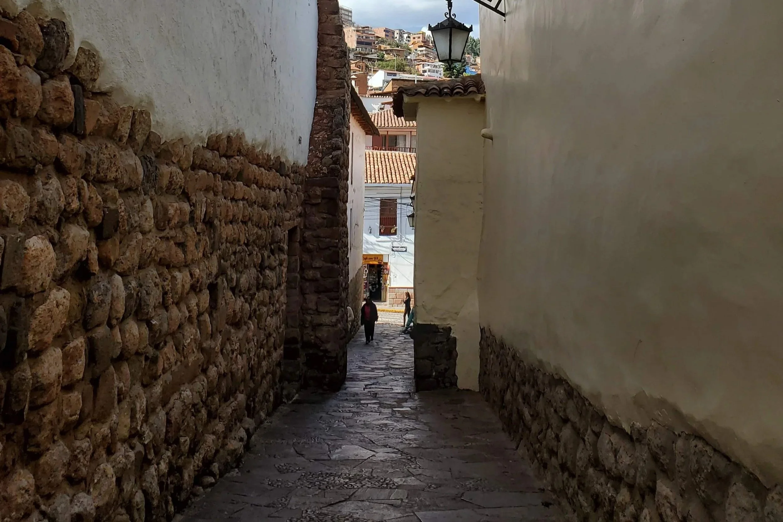 Wandering through narrow, ancient stone alleyways toward red-tiled hillside views in historic Cusco, Peru.