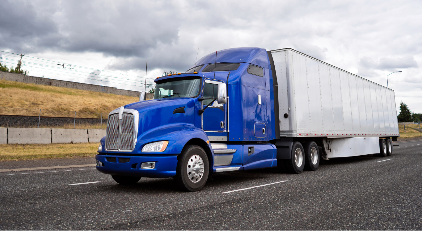 A large blue semi-truck driving on a highway under cloudy skies.