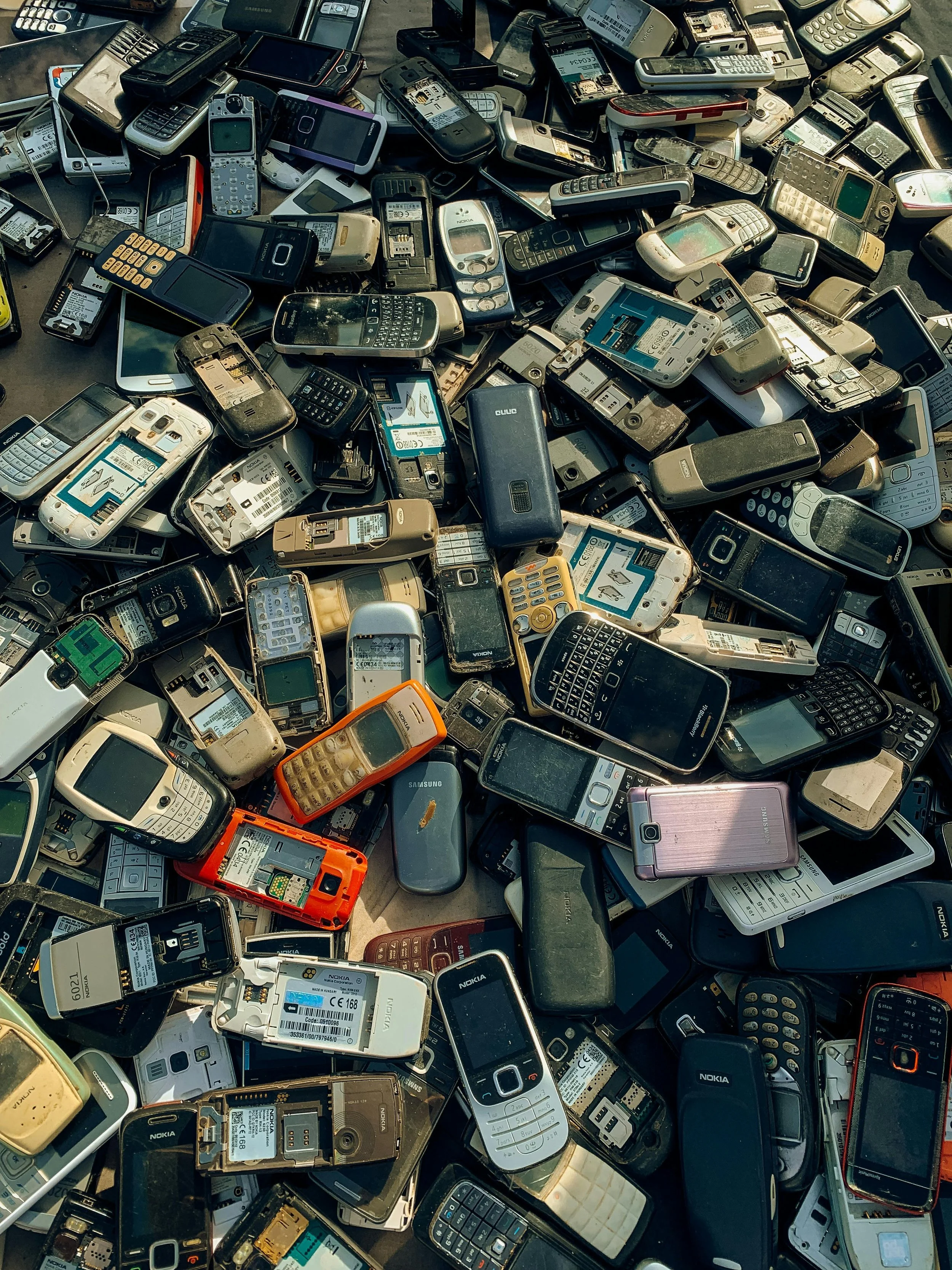 A large pile of old and broken mobile phones and cell phones, some with batteries and screens exposed.