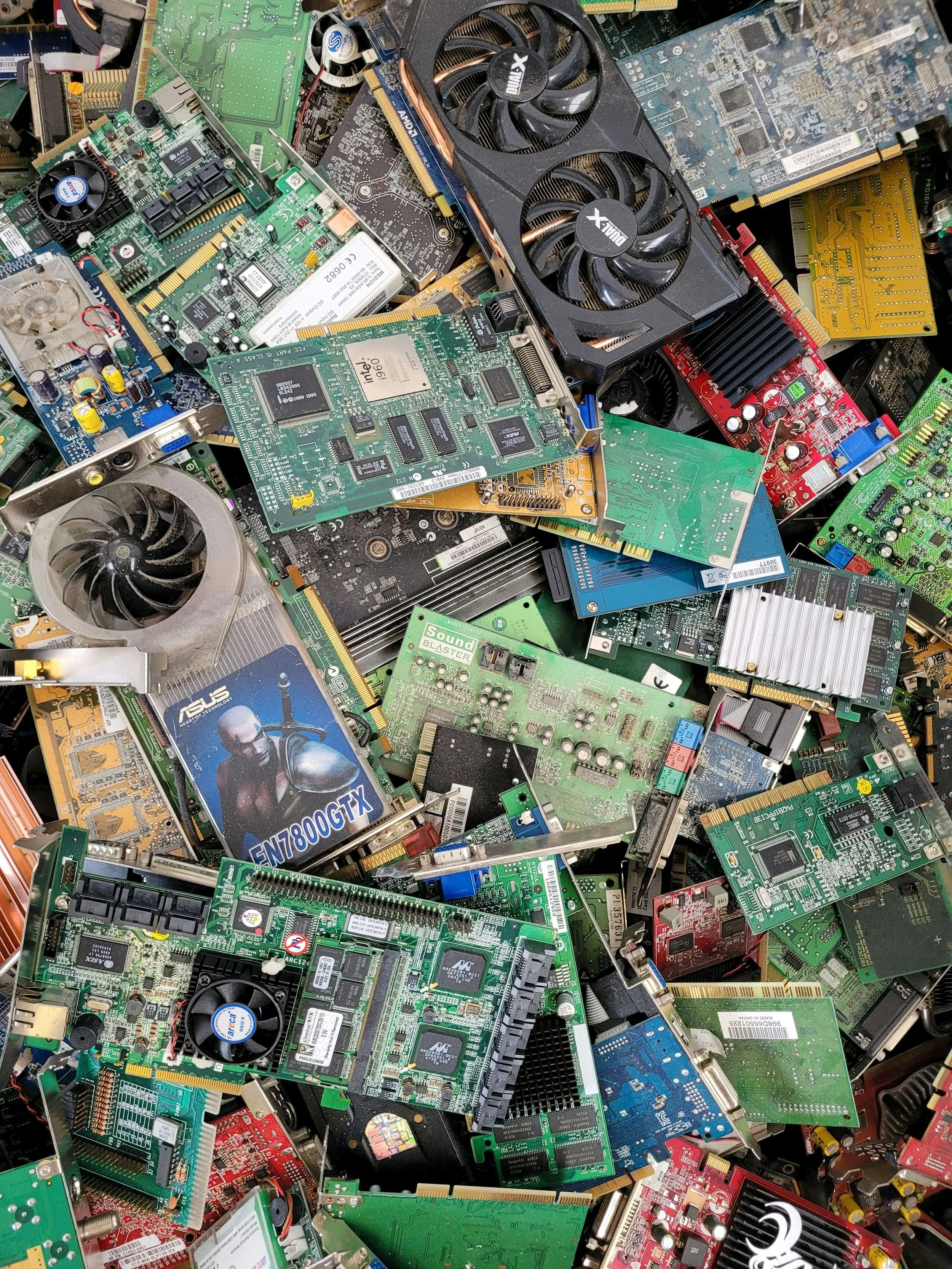 A pile of various computer hardware components including circuit boards, graphics cards, and other electronic parts.