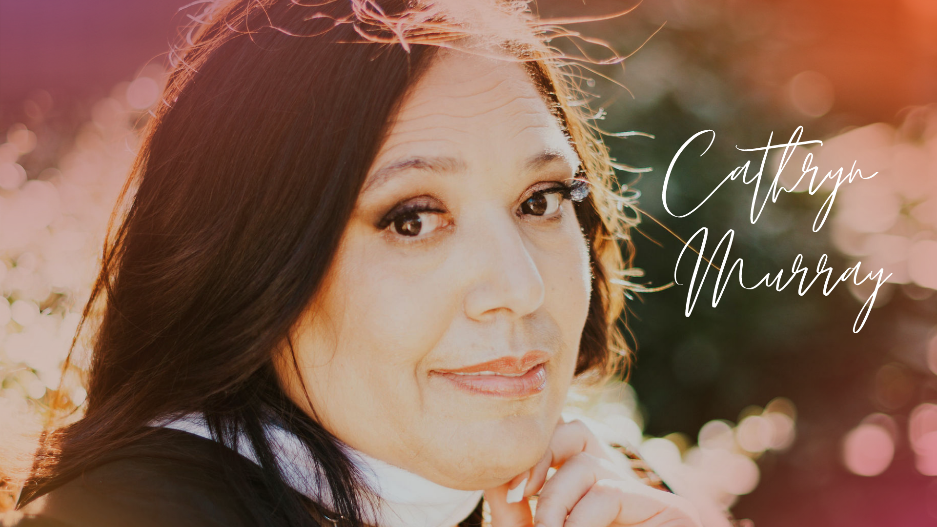 Close-up portrait of a woman with dark hair, light makeup, and a gentle smile, outdoors with pink and white flowers in the background. The image features the name Catherine Murray written in elegant white script.