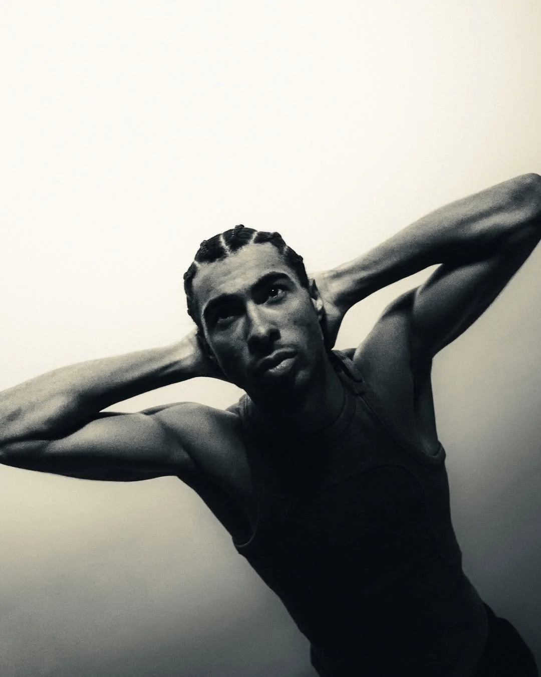 Black and white photo of a person with braided hair leaning back with hands behind their head.