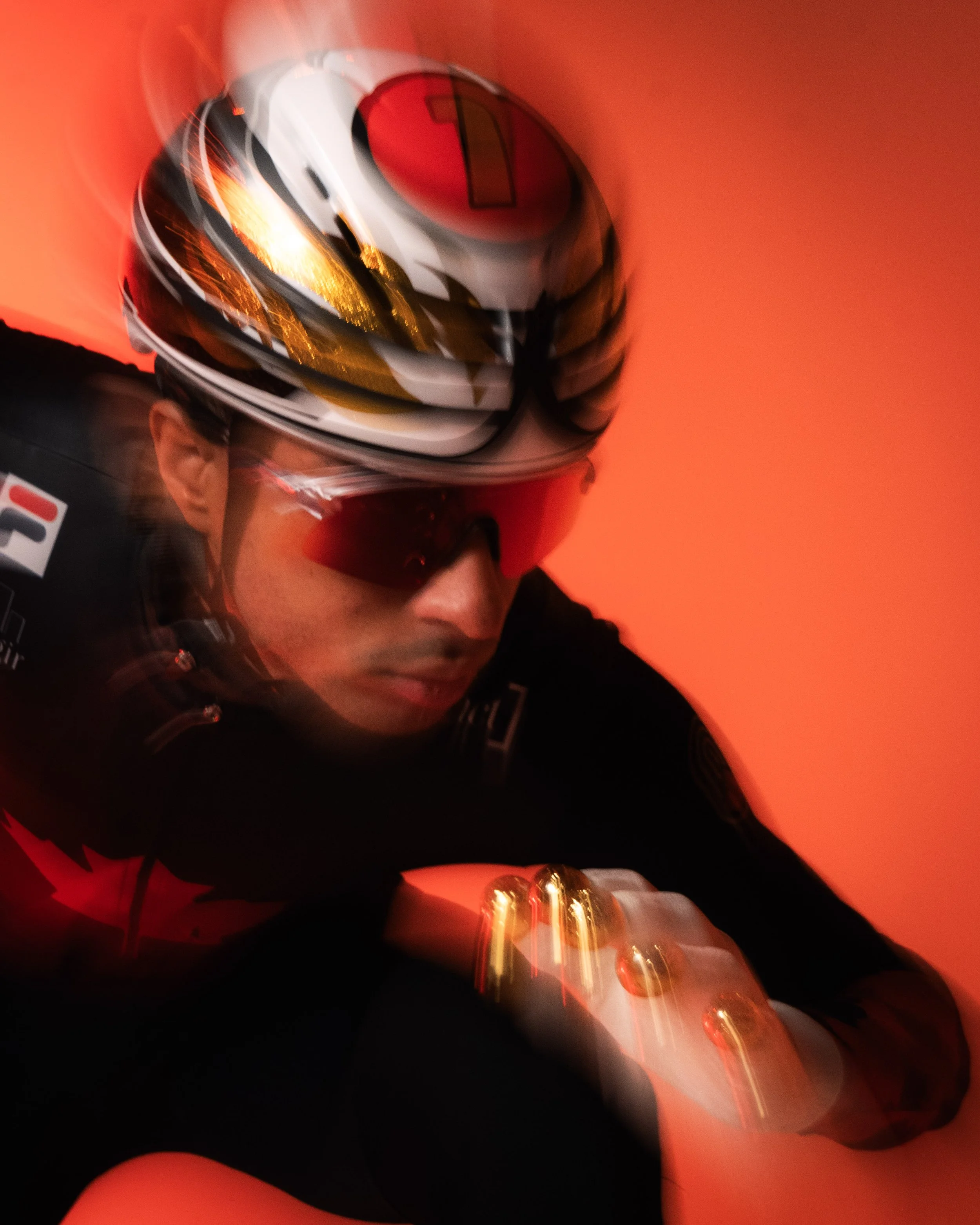 Close-up of a person wearing a racing helmet with a red, black, and white design and a dark racing suit, against a predominantly red background.